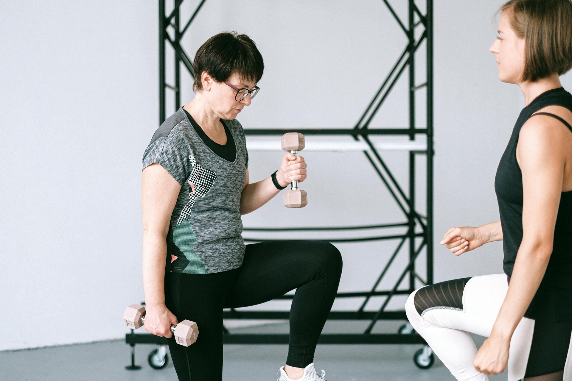 an older woman lifts small weights with instruction from a female coach