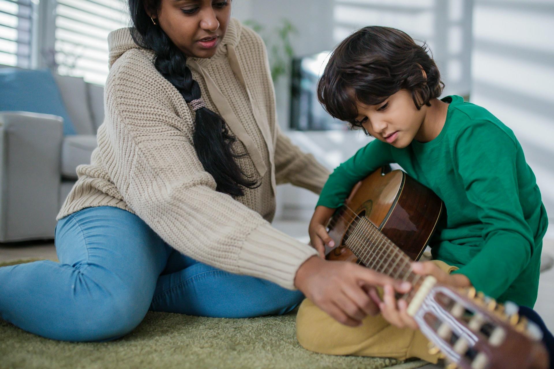 A woman teaching a young child to play guitar.