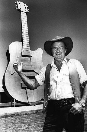 Slim Dusty in a black and white photo standing next to the big "golden guitar"