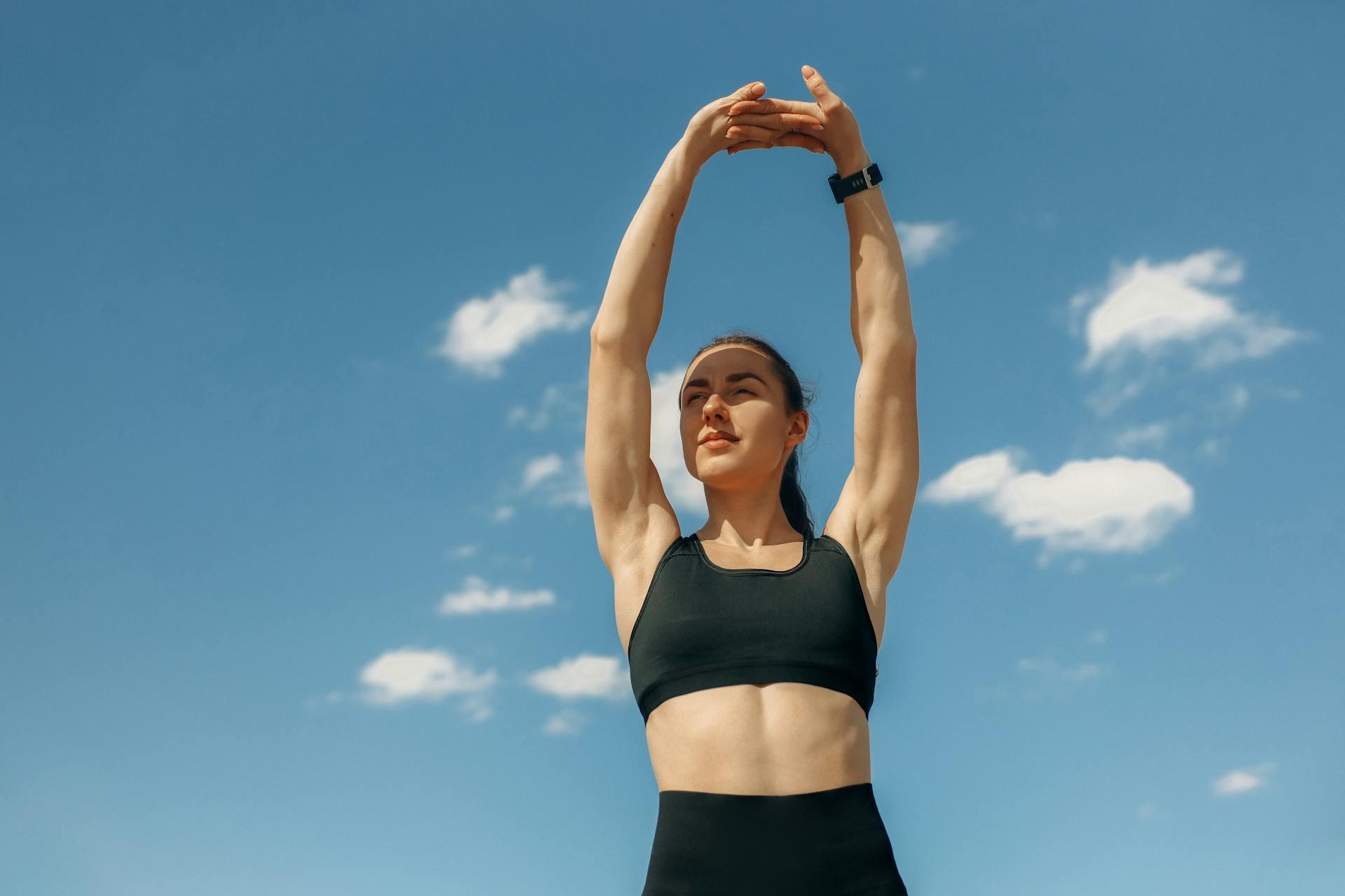 a woman wearing a black workout outfit stretching her arms up to the blue sky