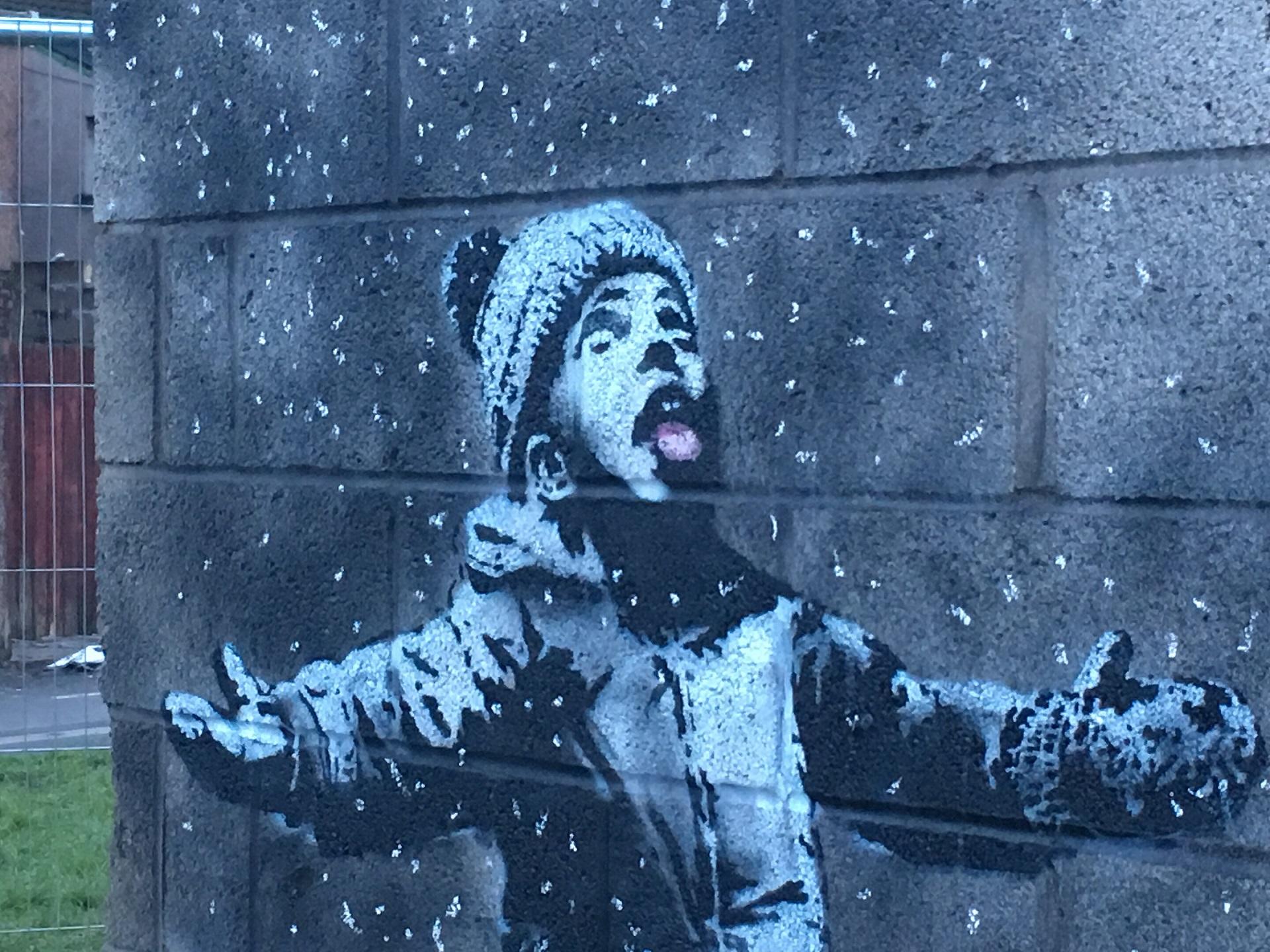 A boy in a hat and mittens sticks his tongue out to catch falling 'snow'.