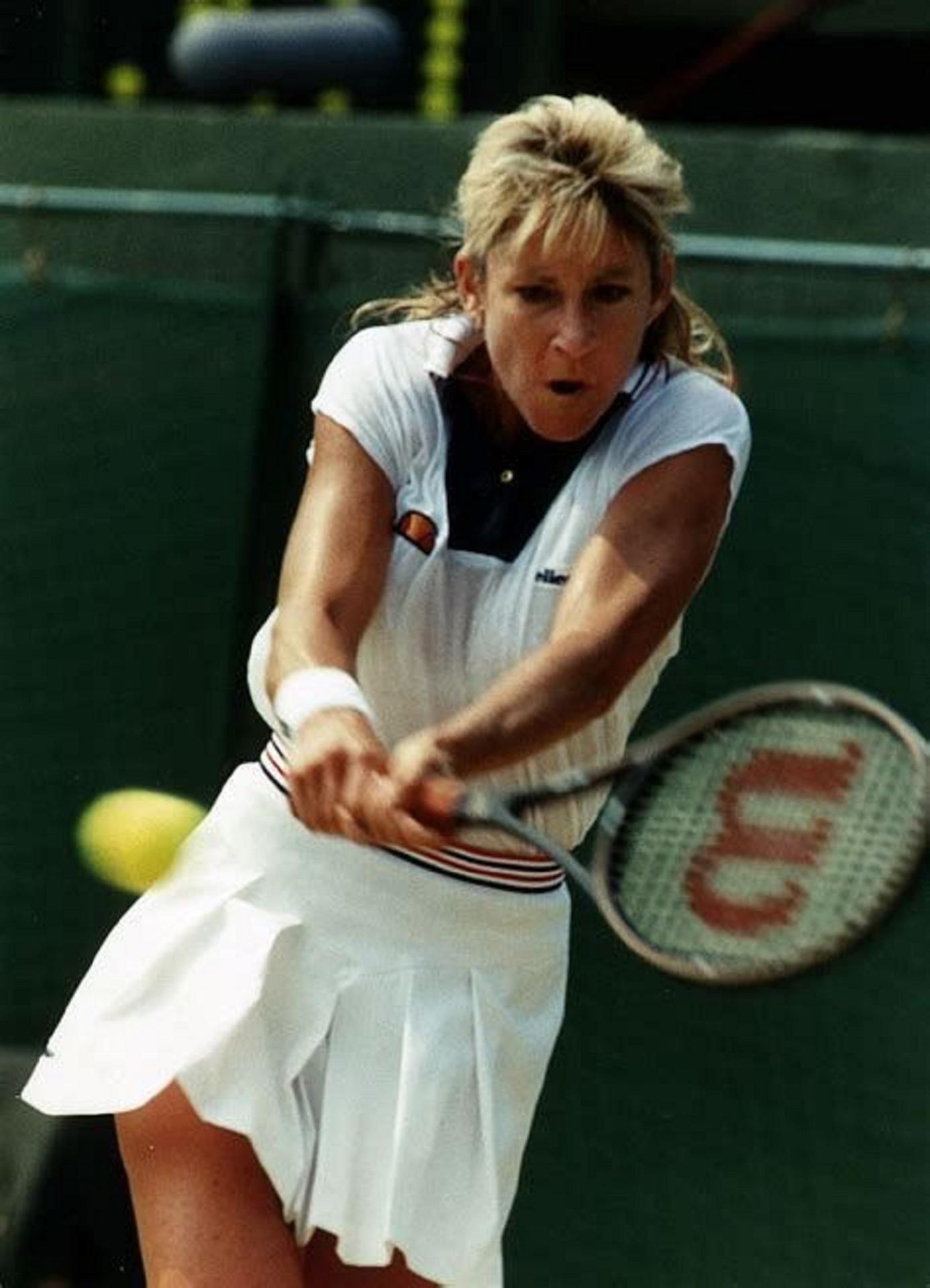 A woman in tennis whites swings a tennis racket towards the incoming tennis ball.