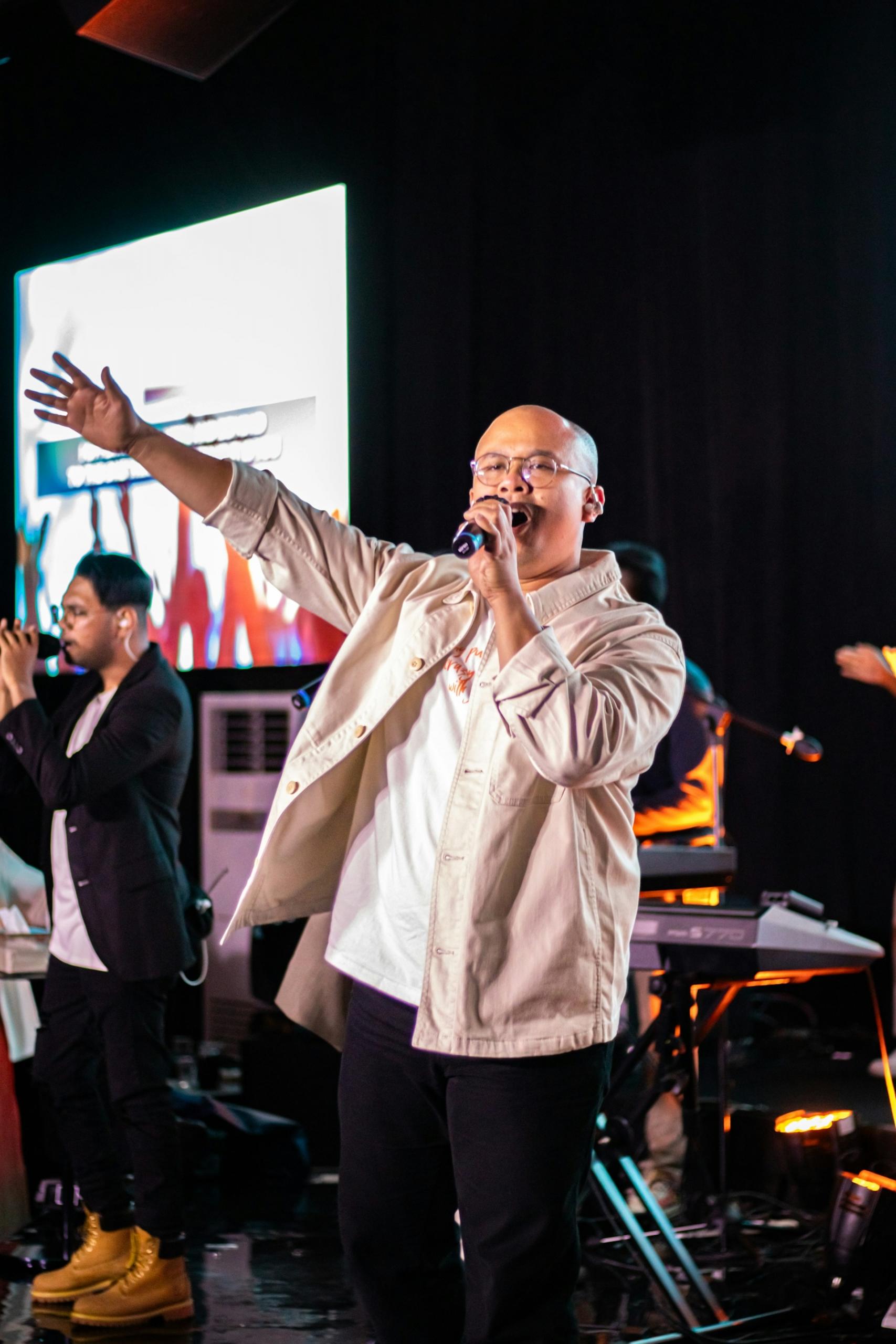 A man with an open shirt showing a white tee shirt holds a microphone. 