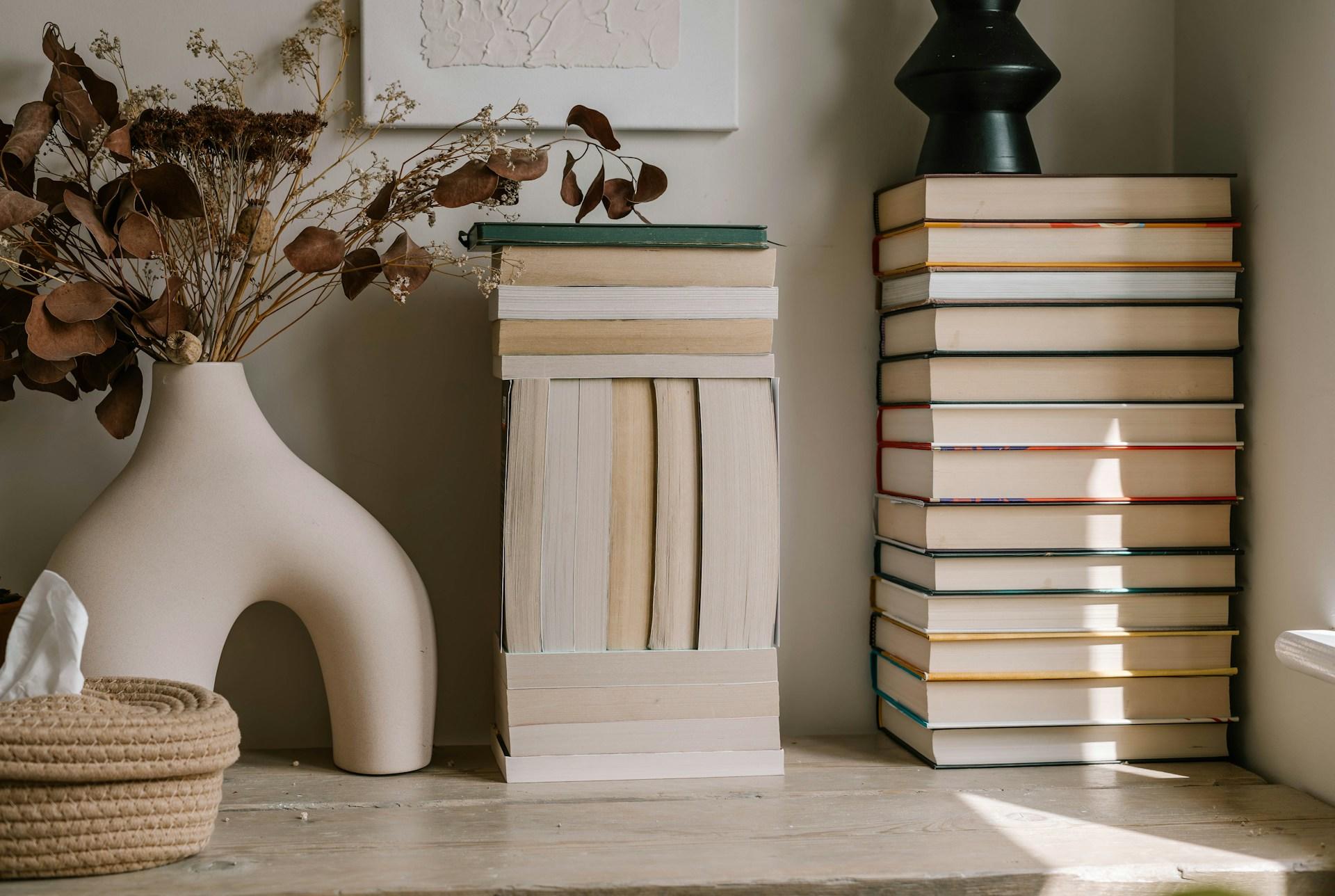A cozy interior corner with stacked books beside a vase with dried plants.