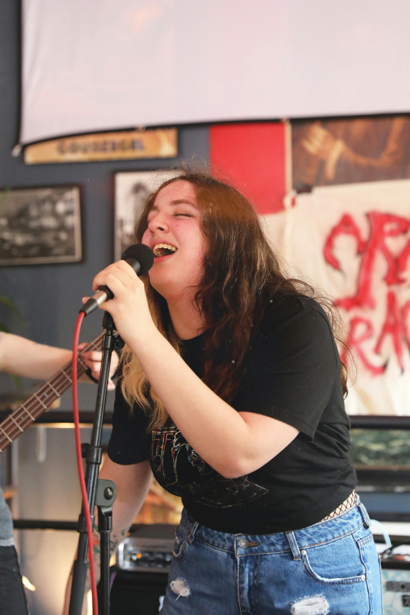 A woman in a black tee shirt holds a microphone on a stand. 