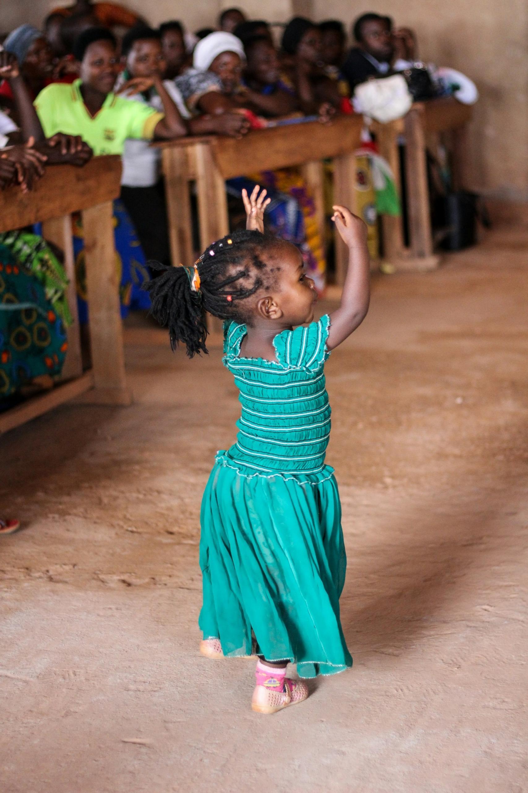 A girl in a green dress with her arms up while dancing. 