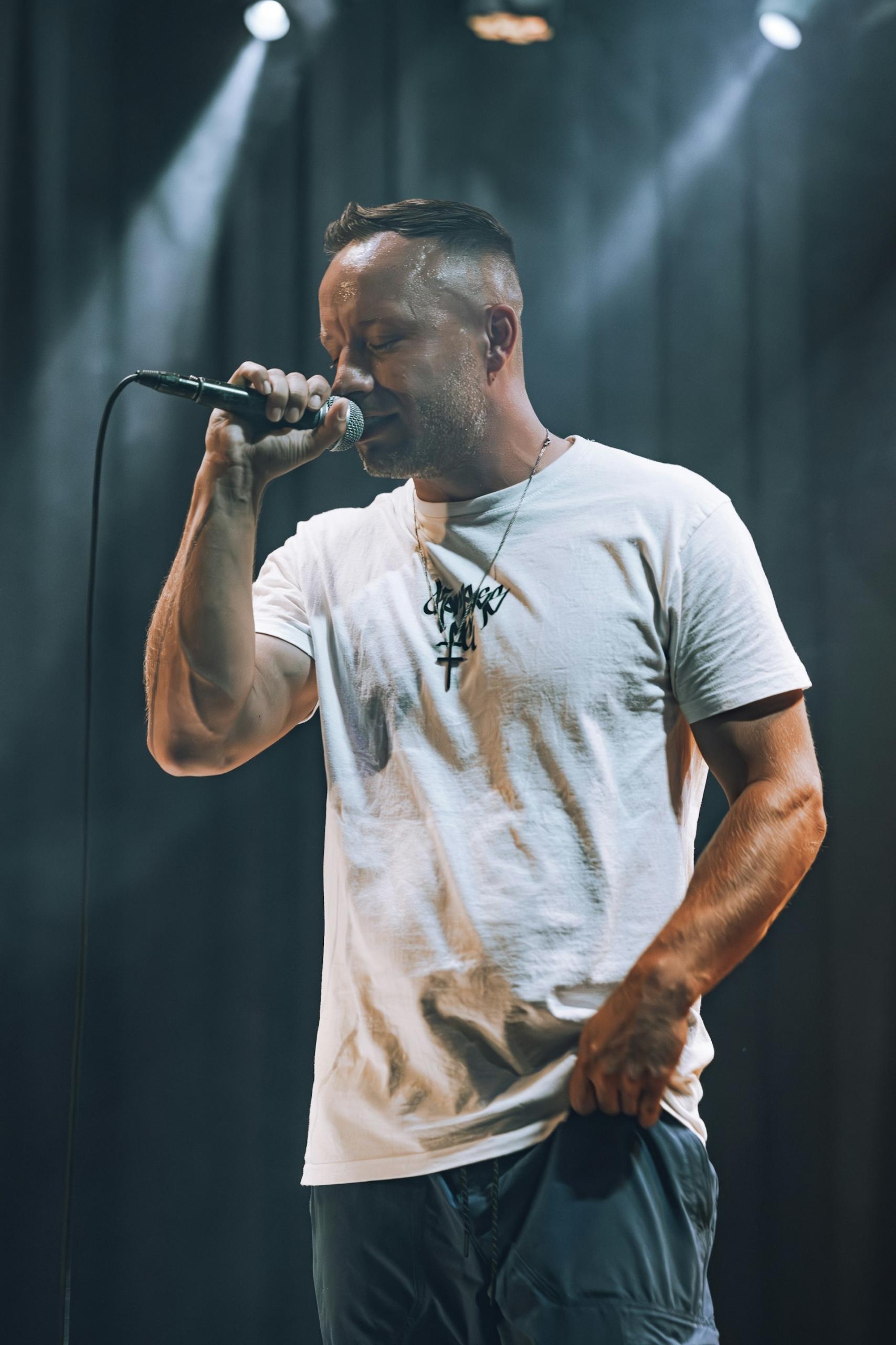 A man in a white shirt holds a microphone on stage.