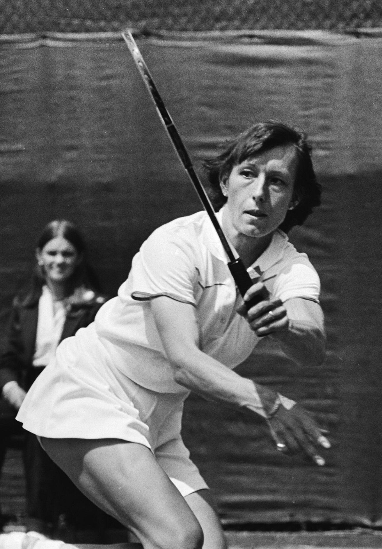 A woman wearing tennis whites swings a tennis racket.