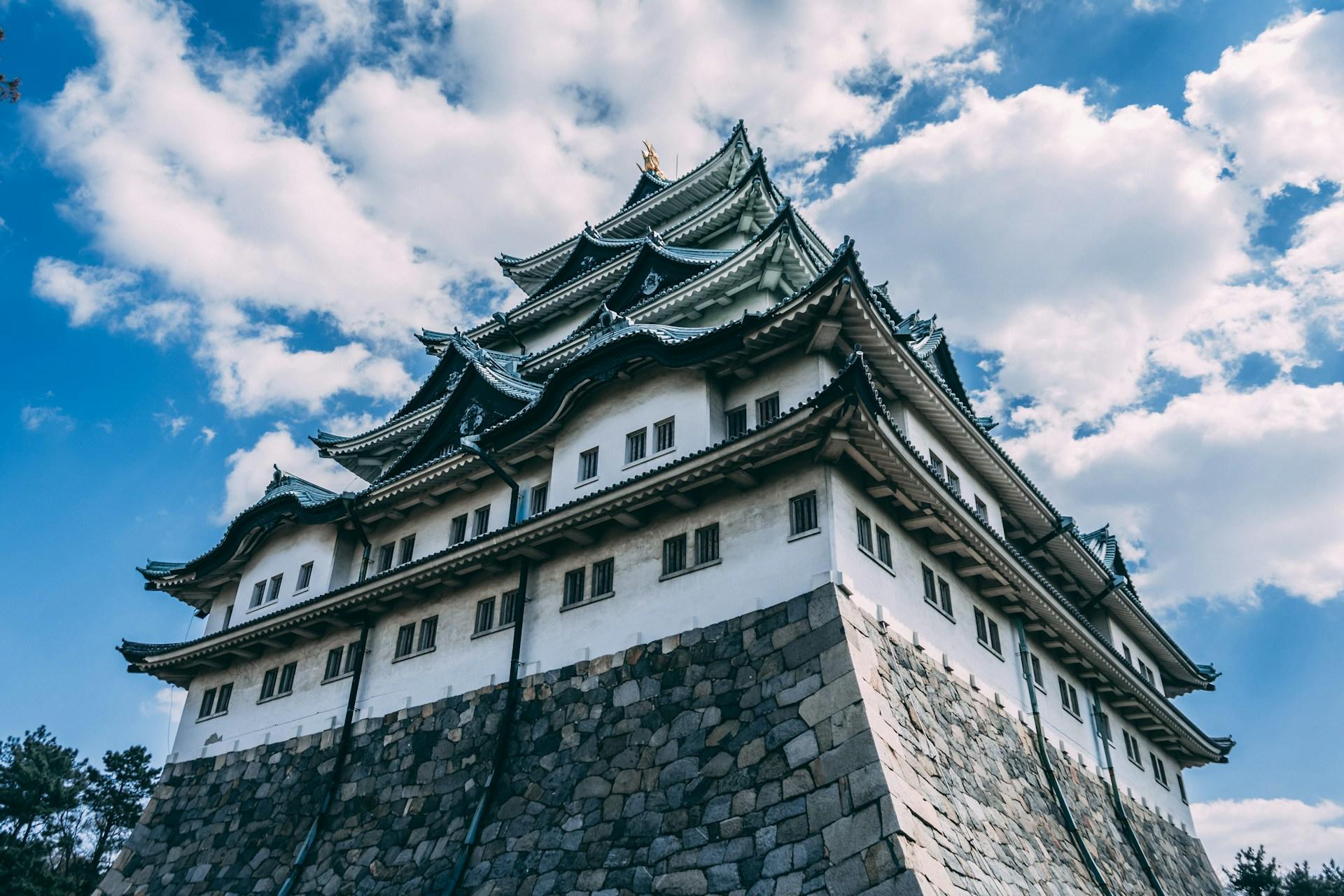 A white building with many peaked roofs on a stone base on a sunny day. 