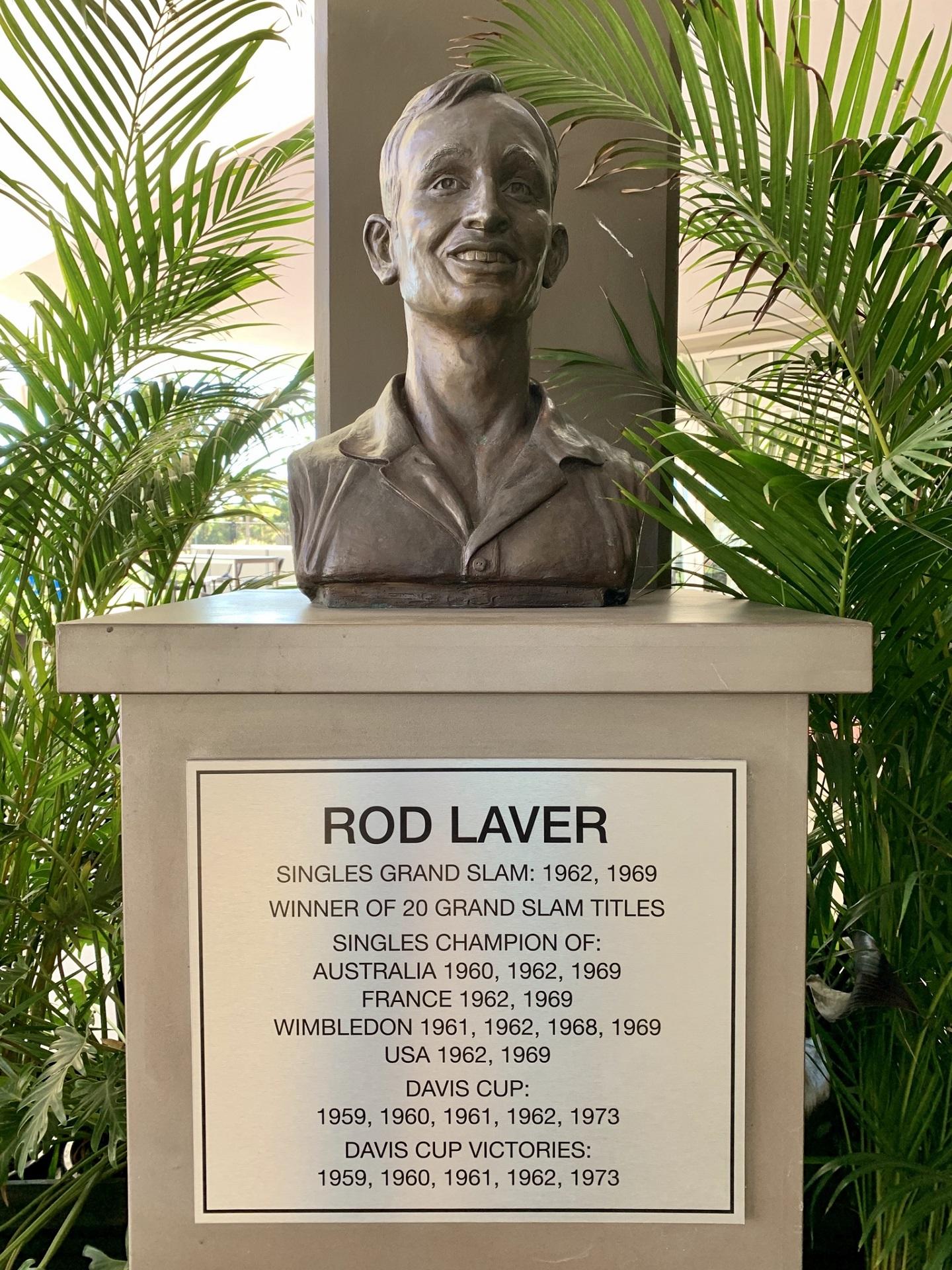 A grey stone bust on a plinth surrounded by palms.