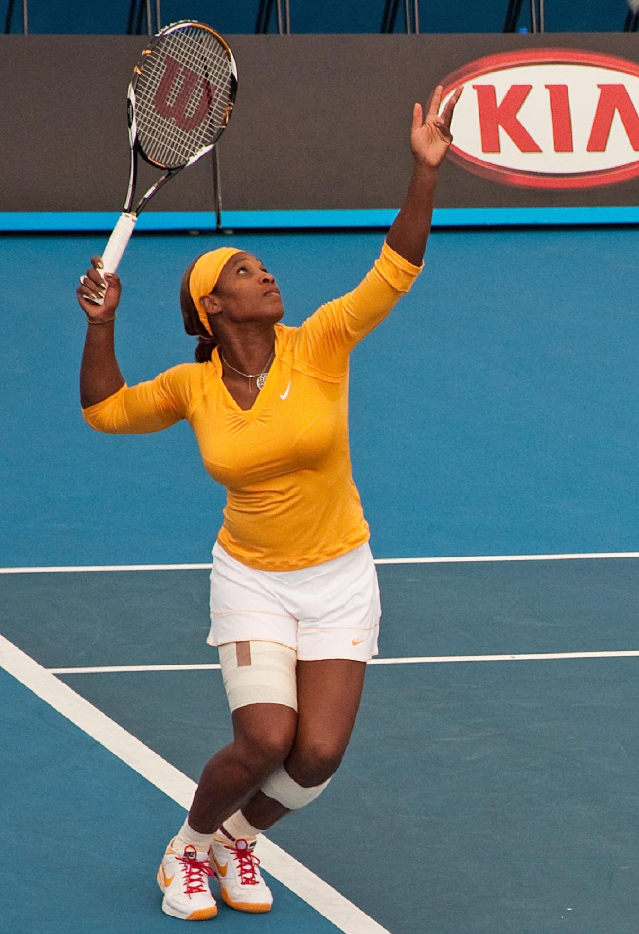 A woman wearing yellow and white holds a tennis racket on a tennis court.