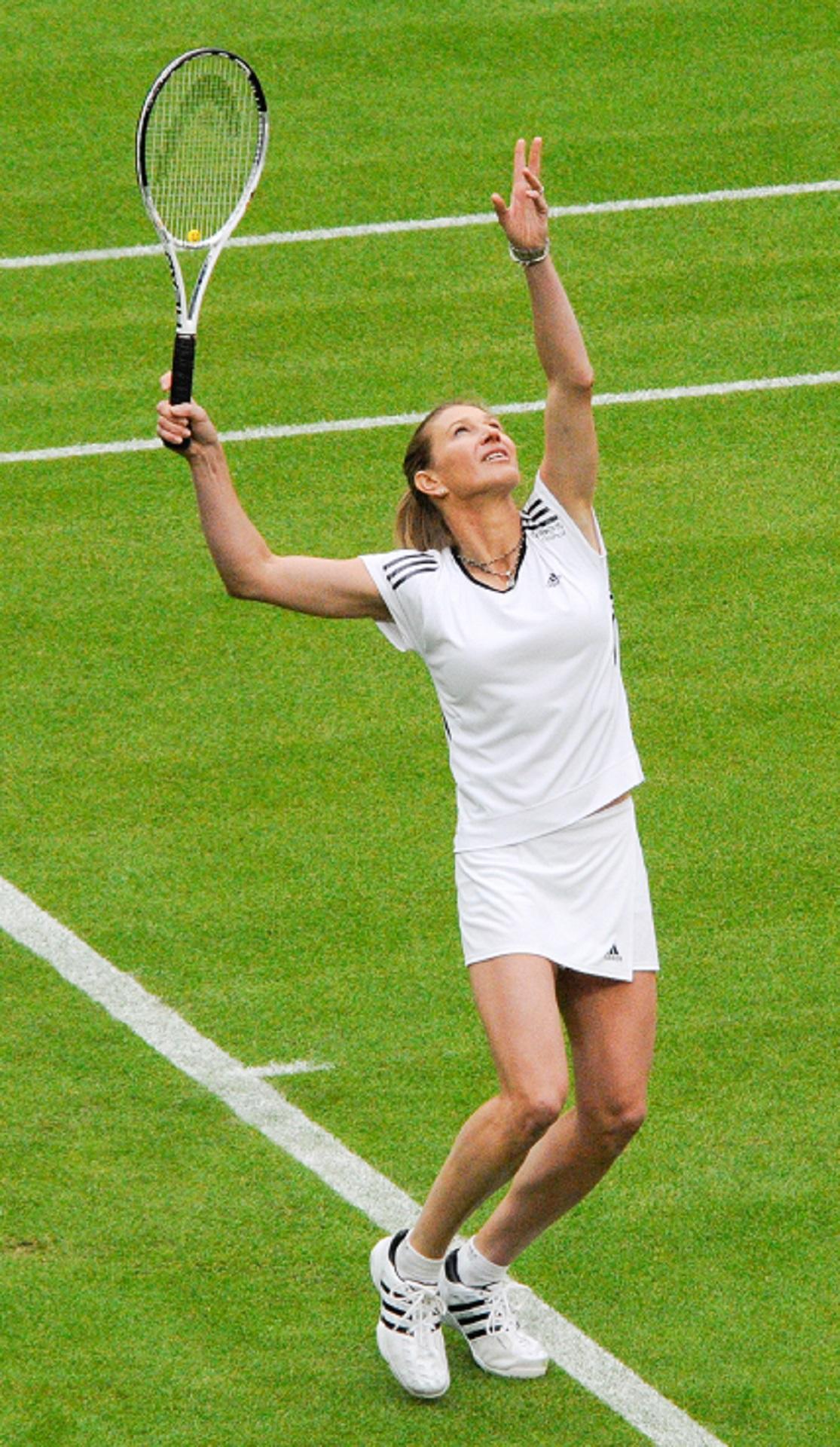 A woman in tennis whites serves a ball on a lawn court.