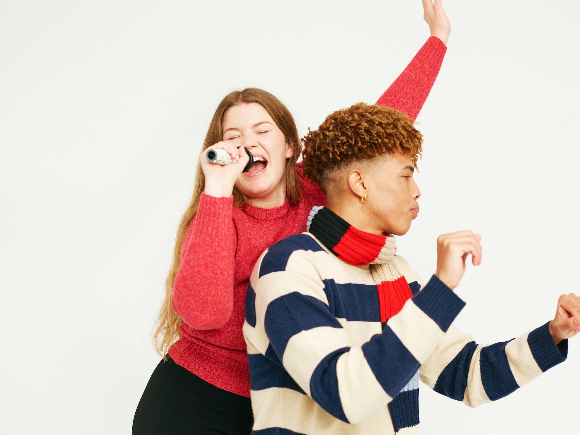 Two people in sweaters posing playfully against a white background.