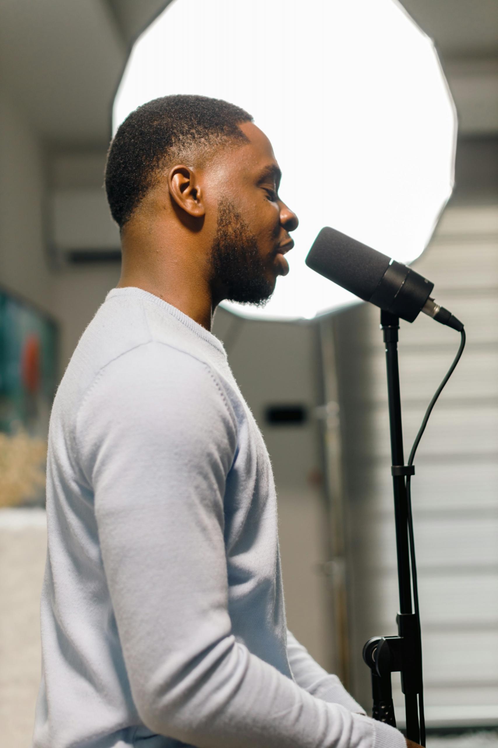 A man in a grey jumper stands behind a microphone in a stand. 