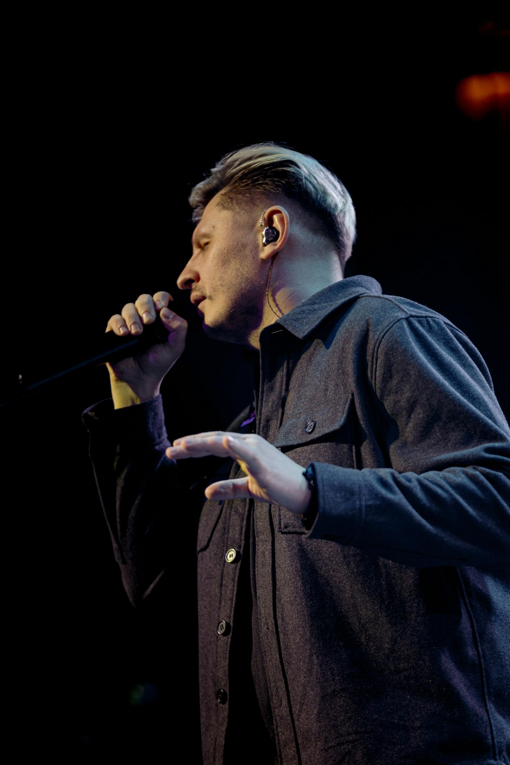 A man in a brown shirt holding a microphone. 