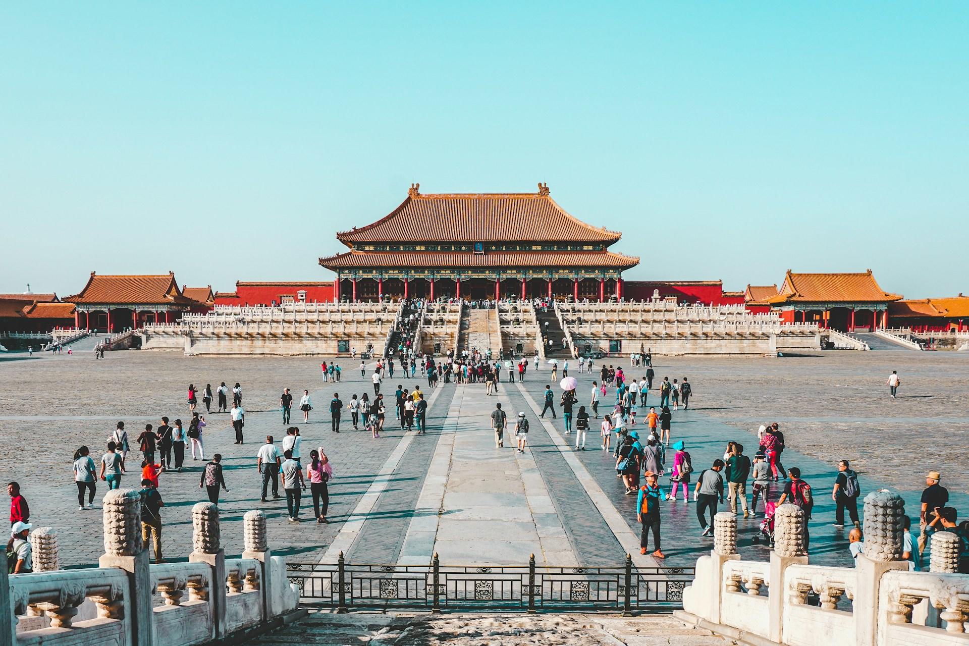 Visitors in Beijing's Forbidden City, featuring historic architecture under a blue sky.