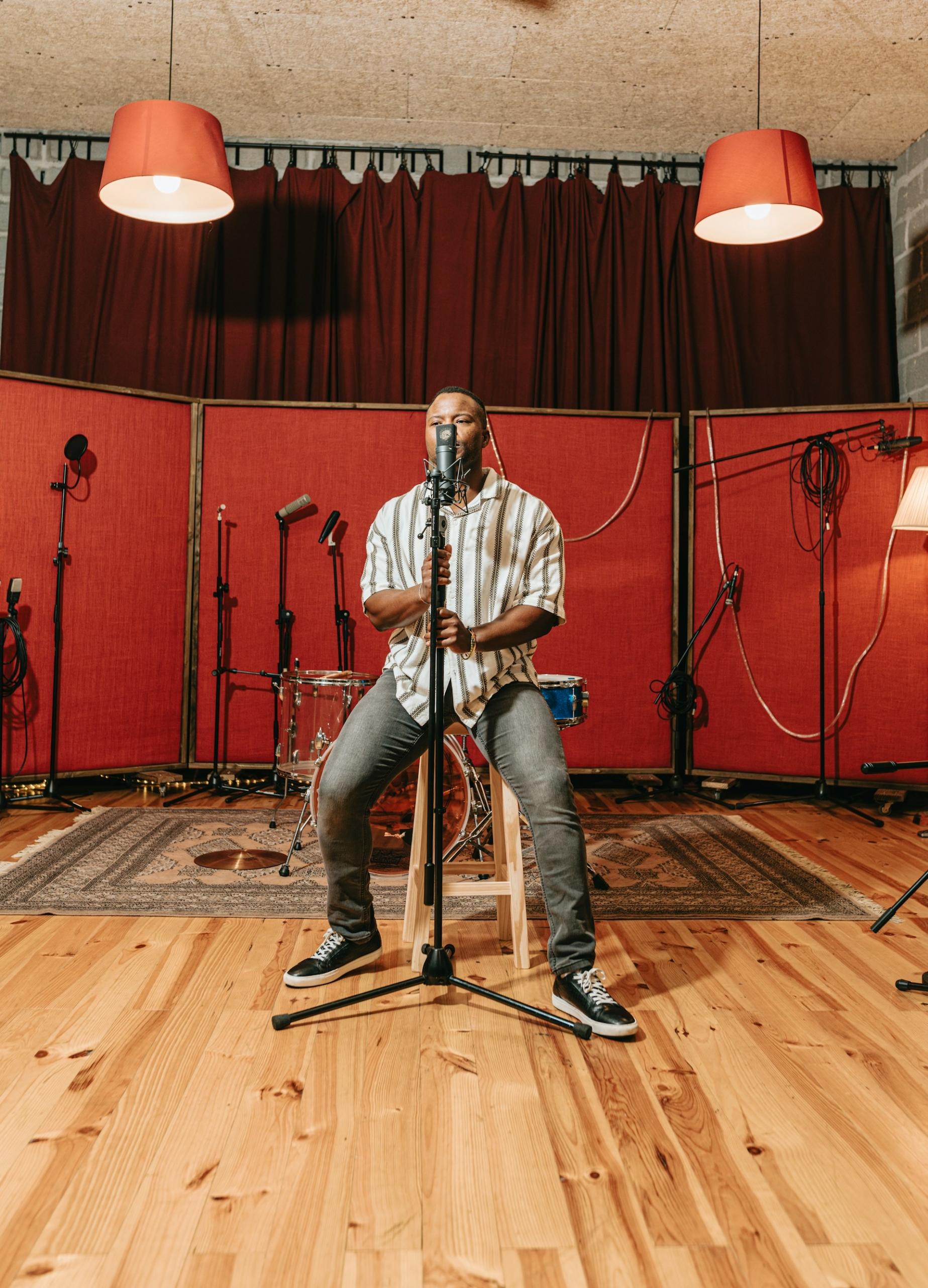 A man wearing casual clothing on a stool behind a microphone stand. 