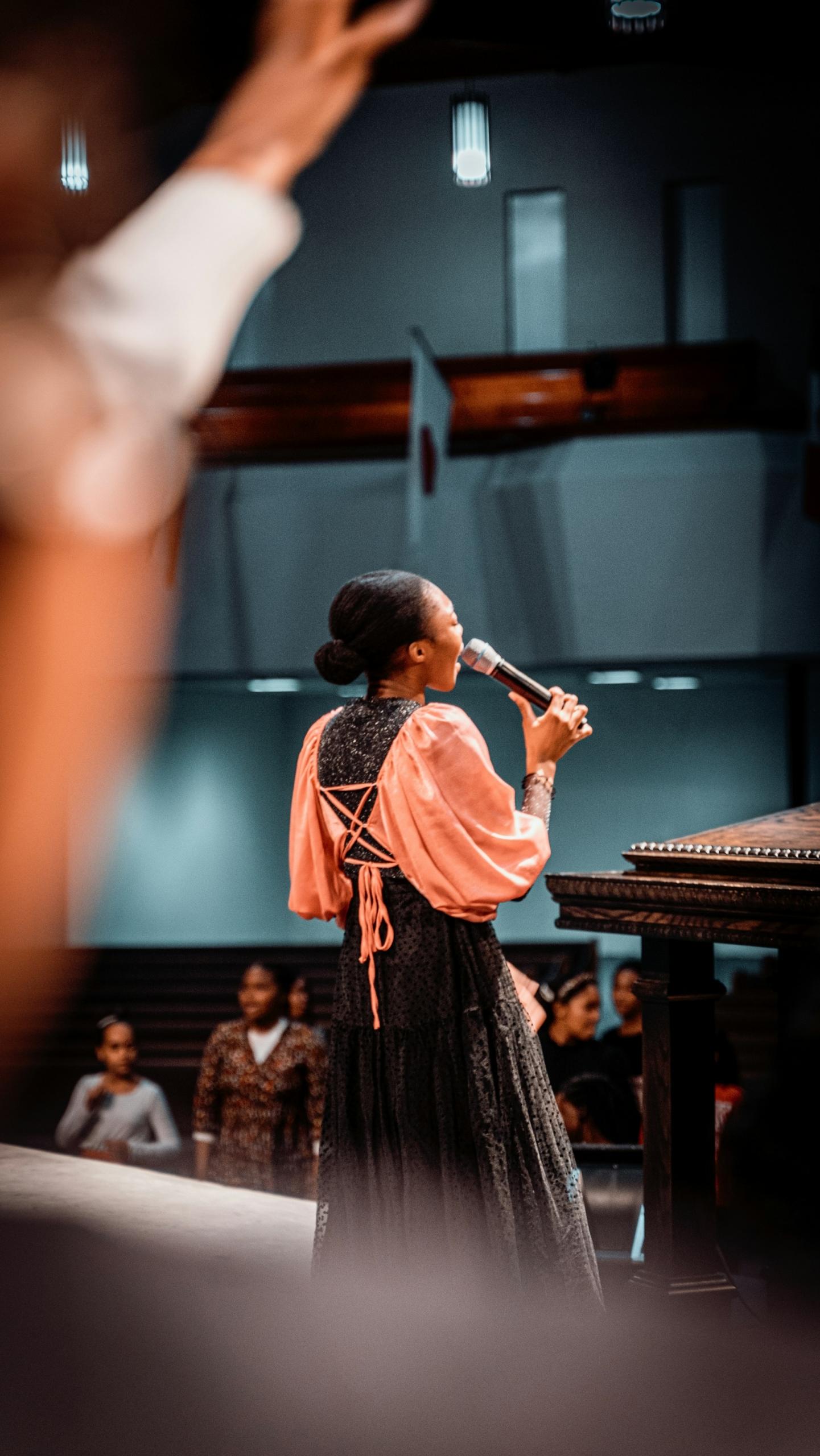 A woman wearing a white and green dress holds a microphone on stage. 
