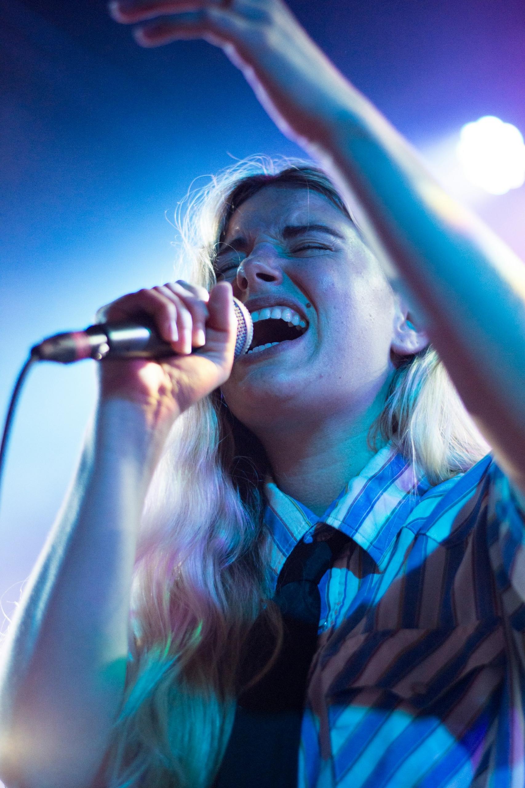 A woman wearing a striped shirt and tie holds a microphone.