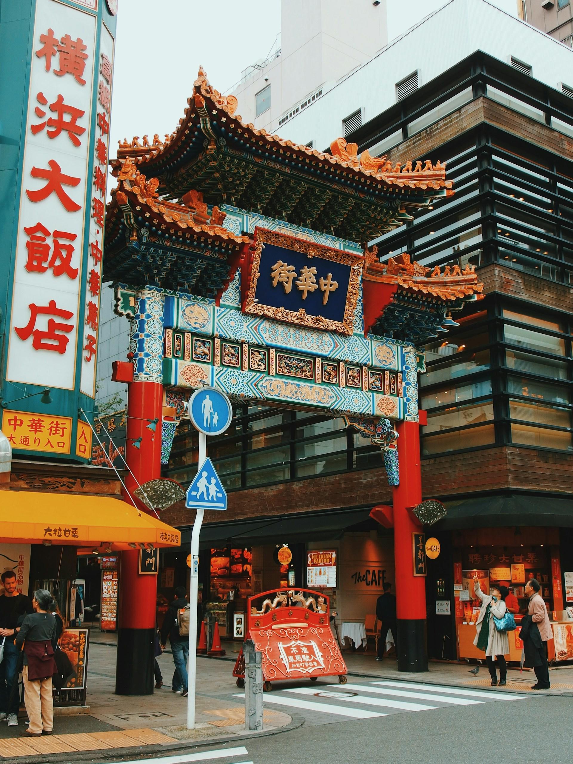A gate and signs with Chinese writing in a city on a cloudy day. 