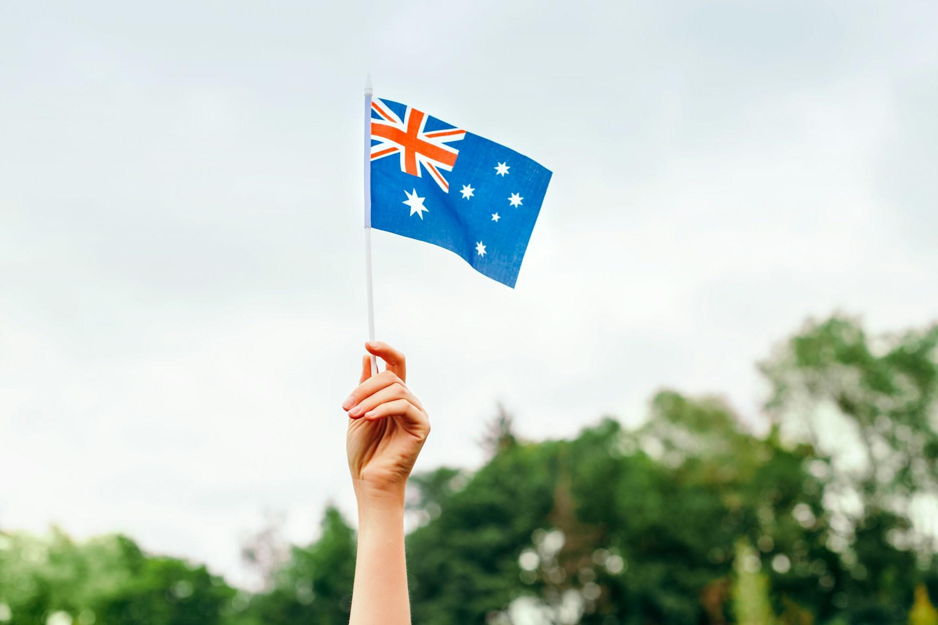 A hand holds up a small Australian flag on a cloudy day.