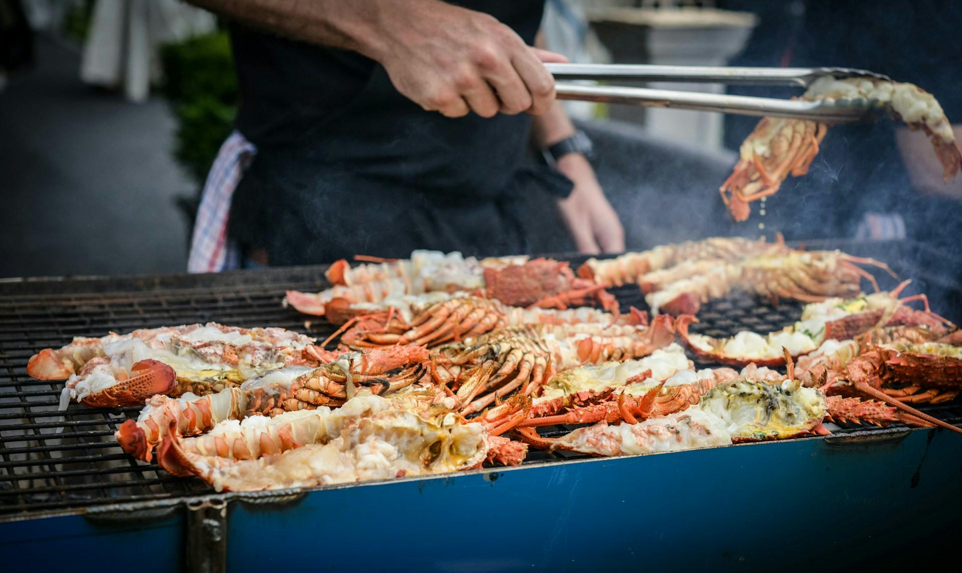 Seafood on a barbecue grill and a person with tongs to turn the food. 