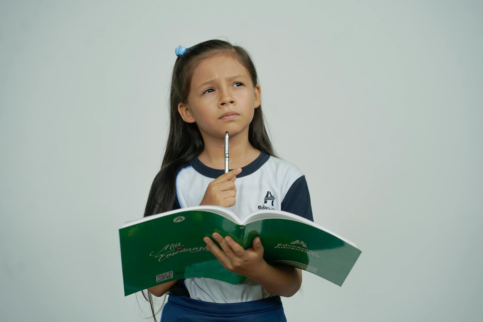 a young girl thinks while holding a pencil and notebook