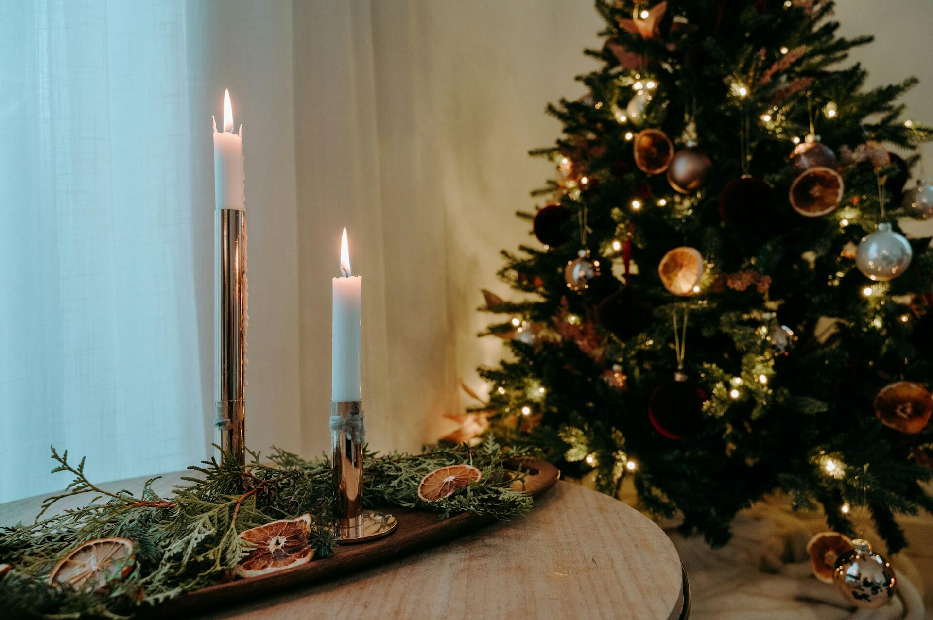 Lit candles on a table with a decorated Christmas tree in the background.