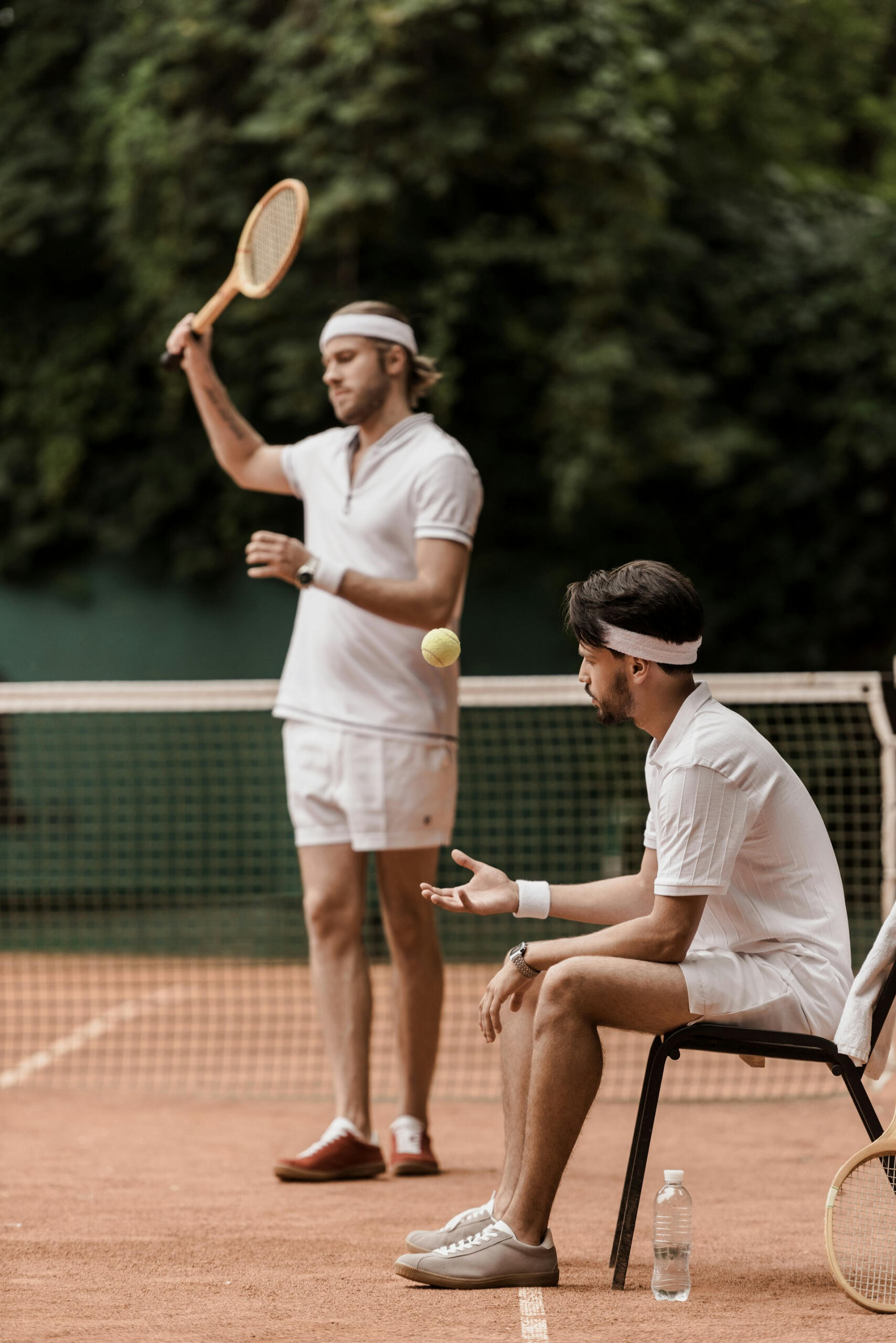 Two men wearing tennis clothes holding rackets on a clay court.