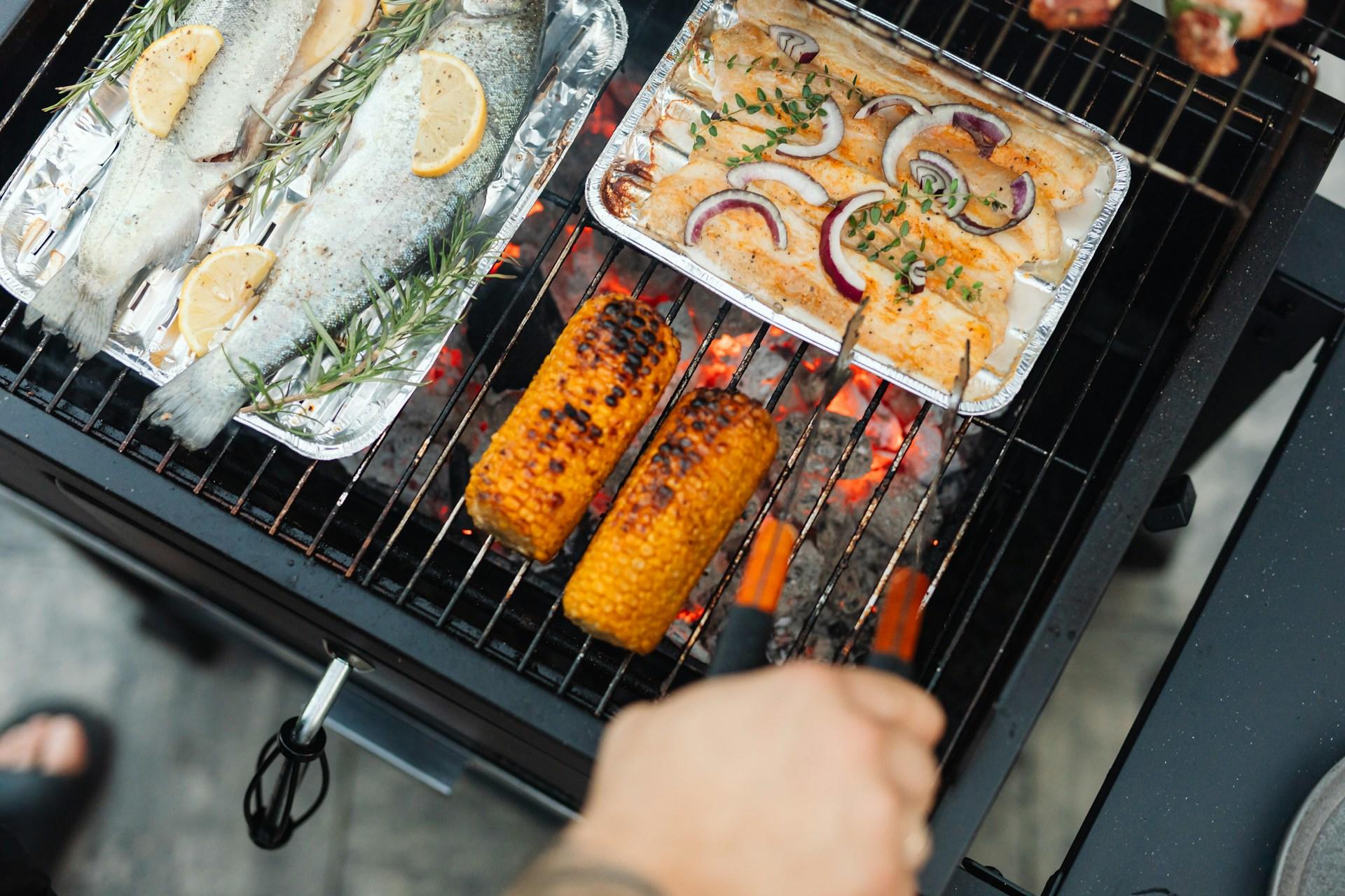 Grilling fish, chicken, and corn on an outdoor barbecue.