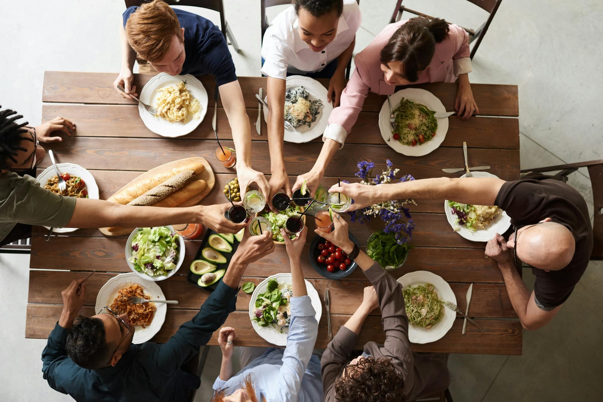 a table filled with plates of food and 8 people clinking glasses together