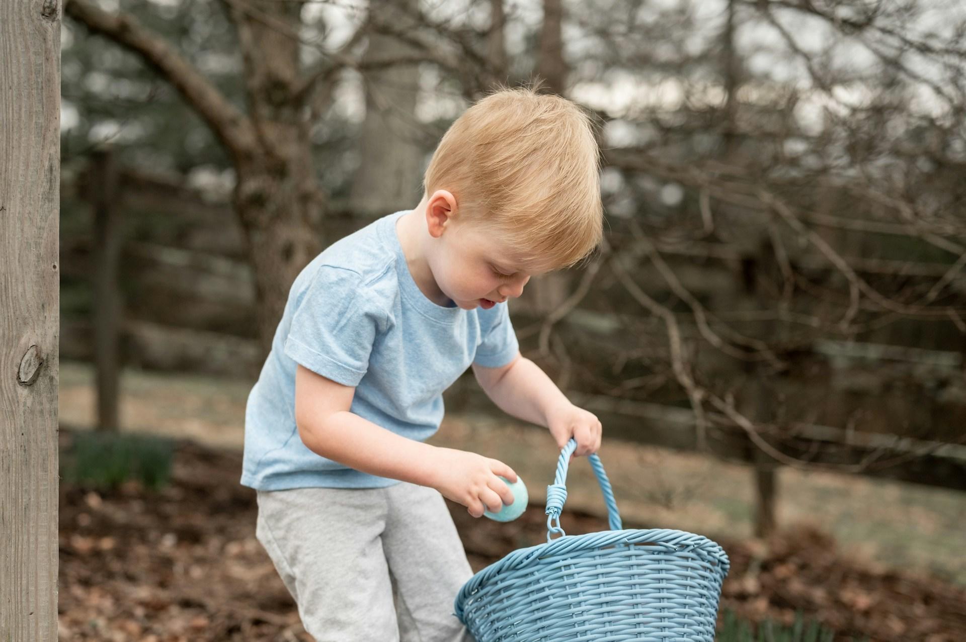 A young boy holding a blue basket outdoors on an autumn day. 