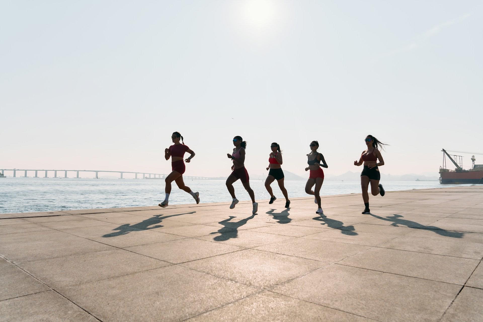Group of runners by the sea with a bridge in the distance.