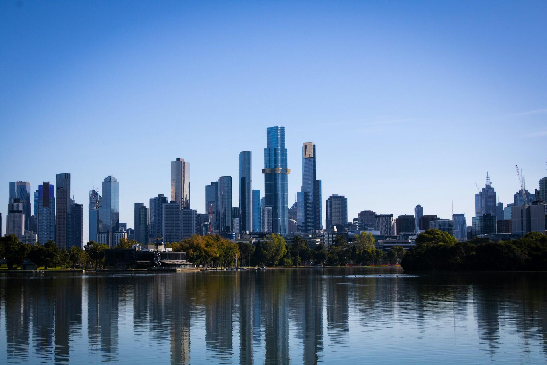 City skyline reflecting on water with clear blue sky.