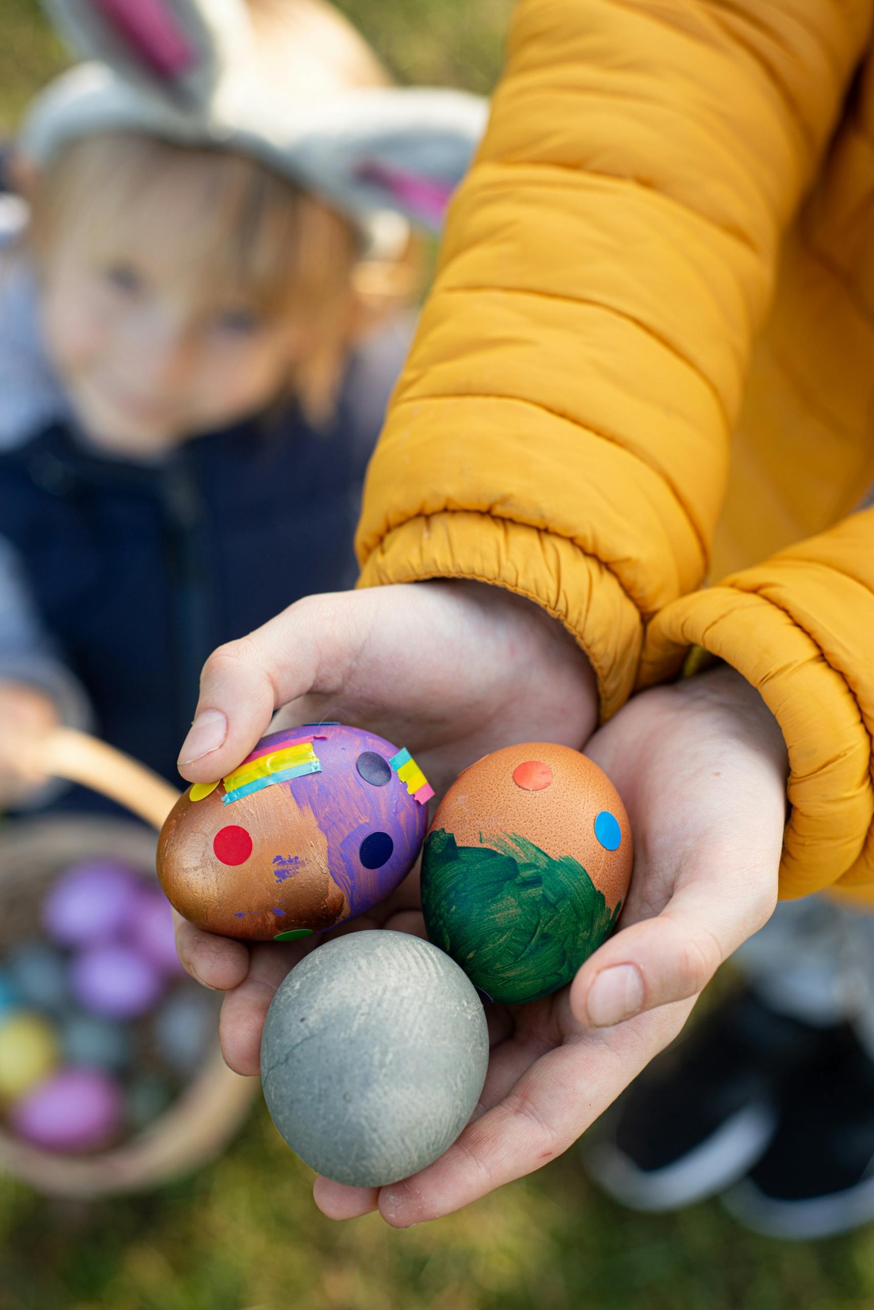 A person wearing a yellow jacket holds Easter eggs in their cupped hands. 