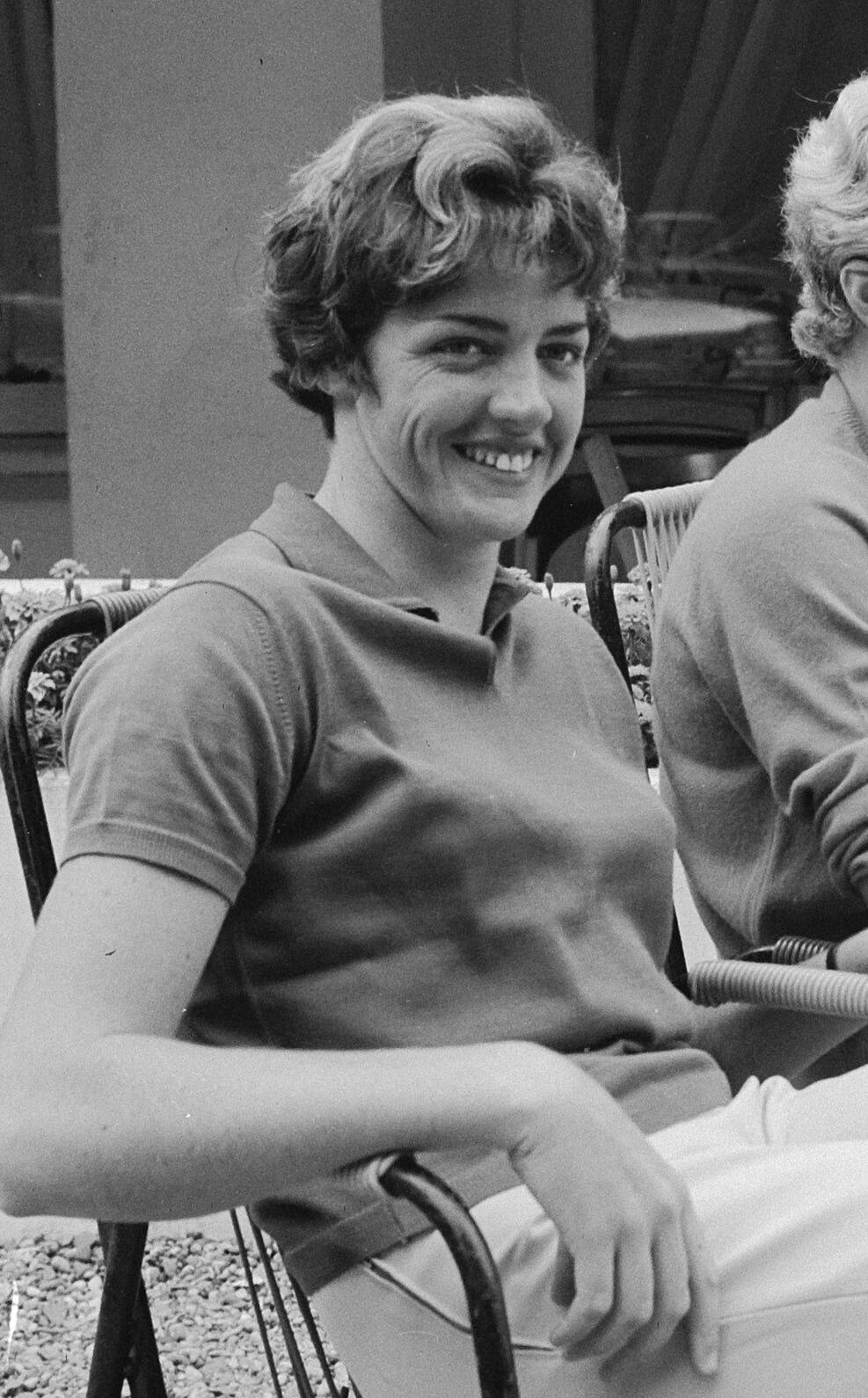 A woman sitting and smiling by a tennis court.