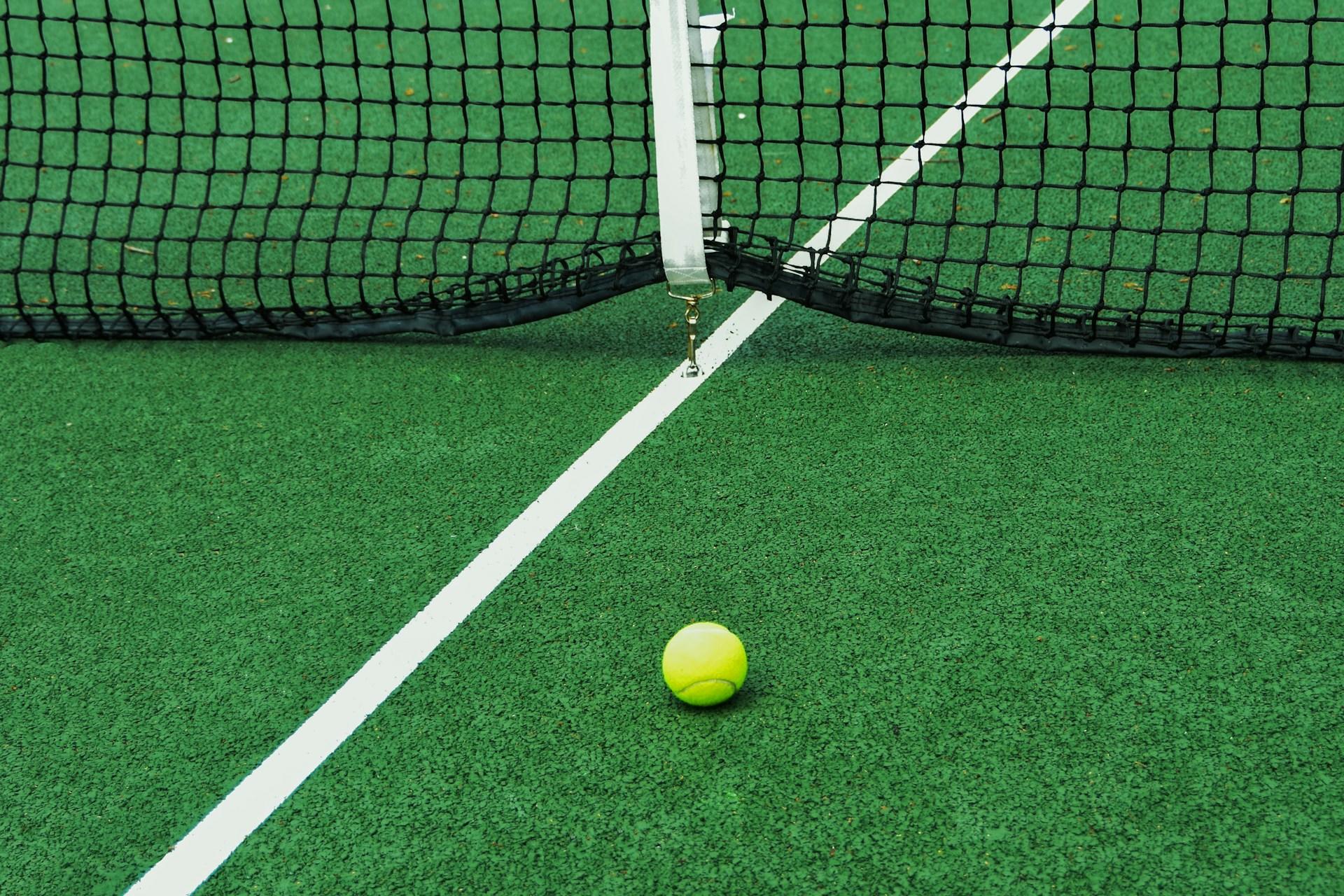 A tennis ball on the ground of a grass court.