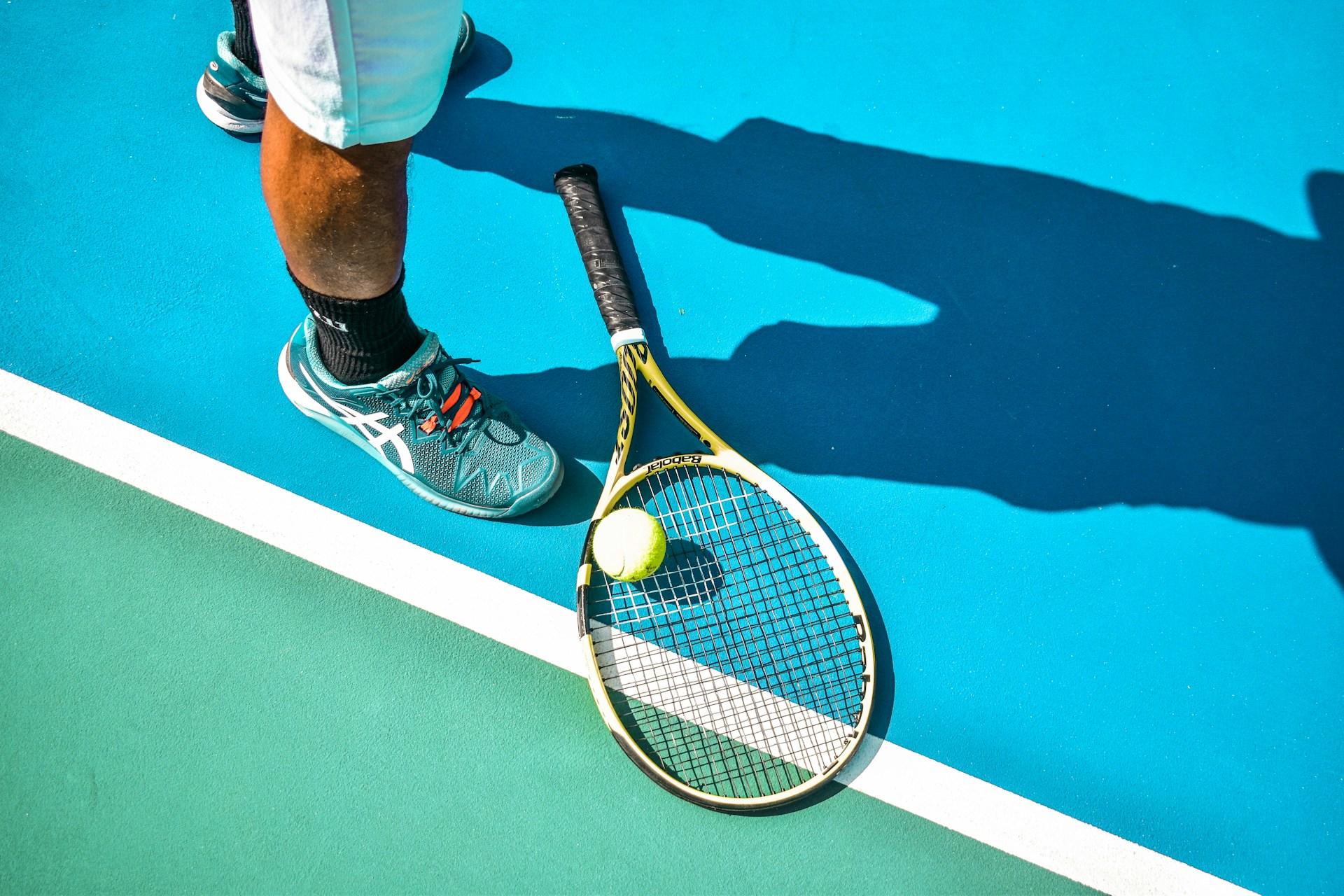 A tennis player's feet and racquet by the baseline of a tennis court.