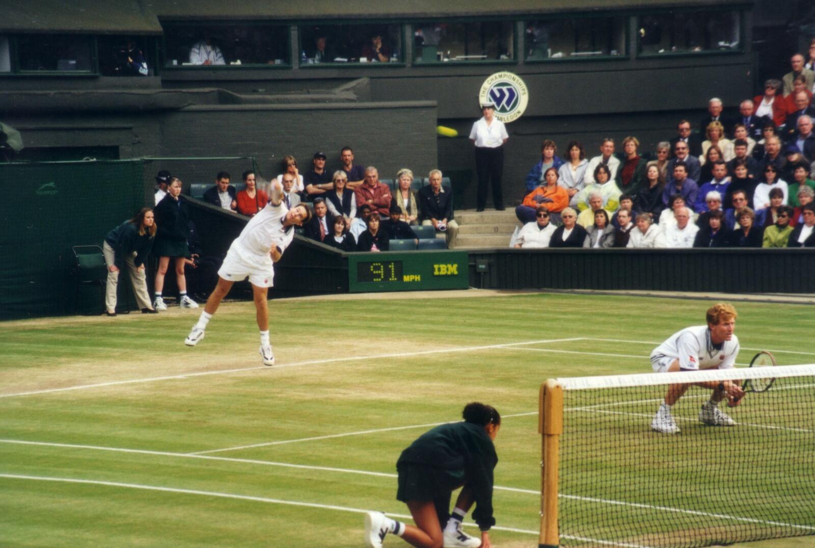 Two men play tennis on a grass court.