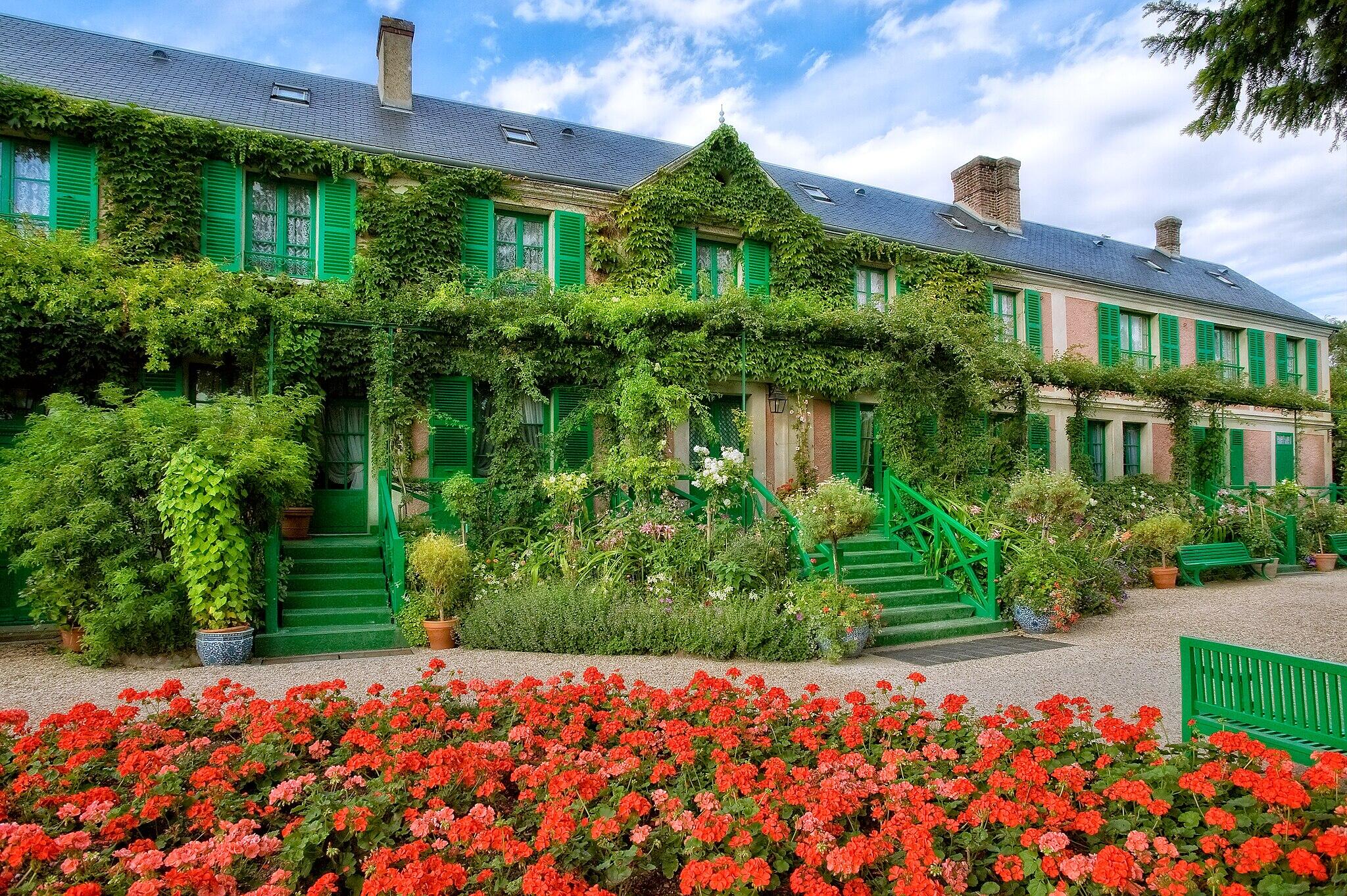 Ivy-covered house with green shutters and lush garden with red flowers.