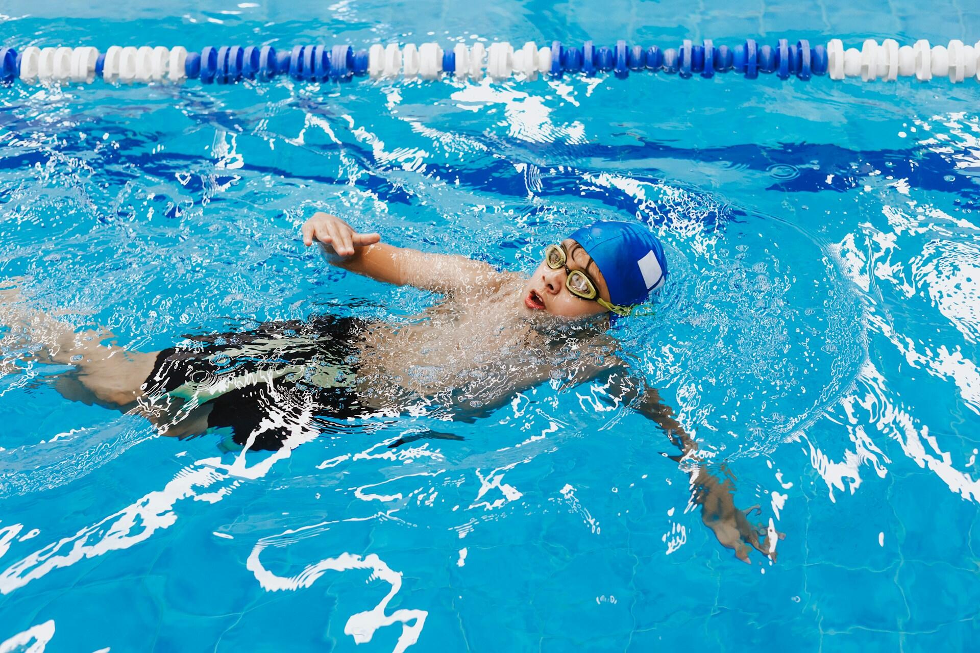 A person wearing a blue swim cap and goggles in a pool.