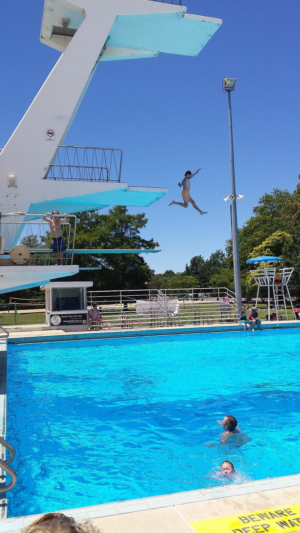 An outdoor swimming pool with diving platform on a sunny day.