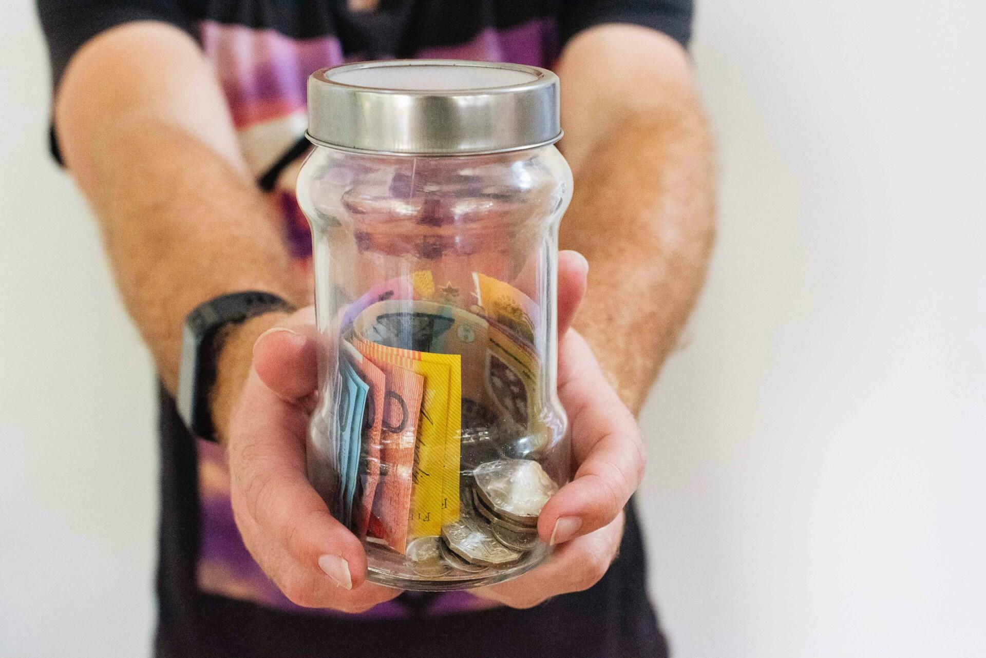 A person holding out a jar of money.