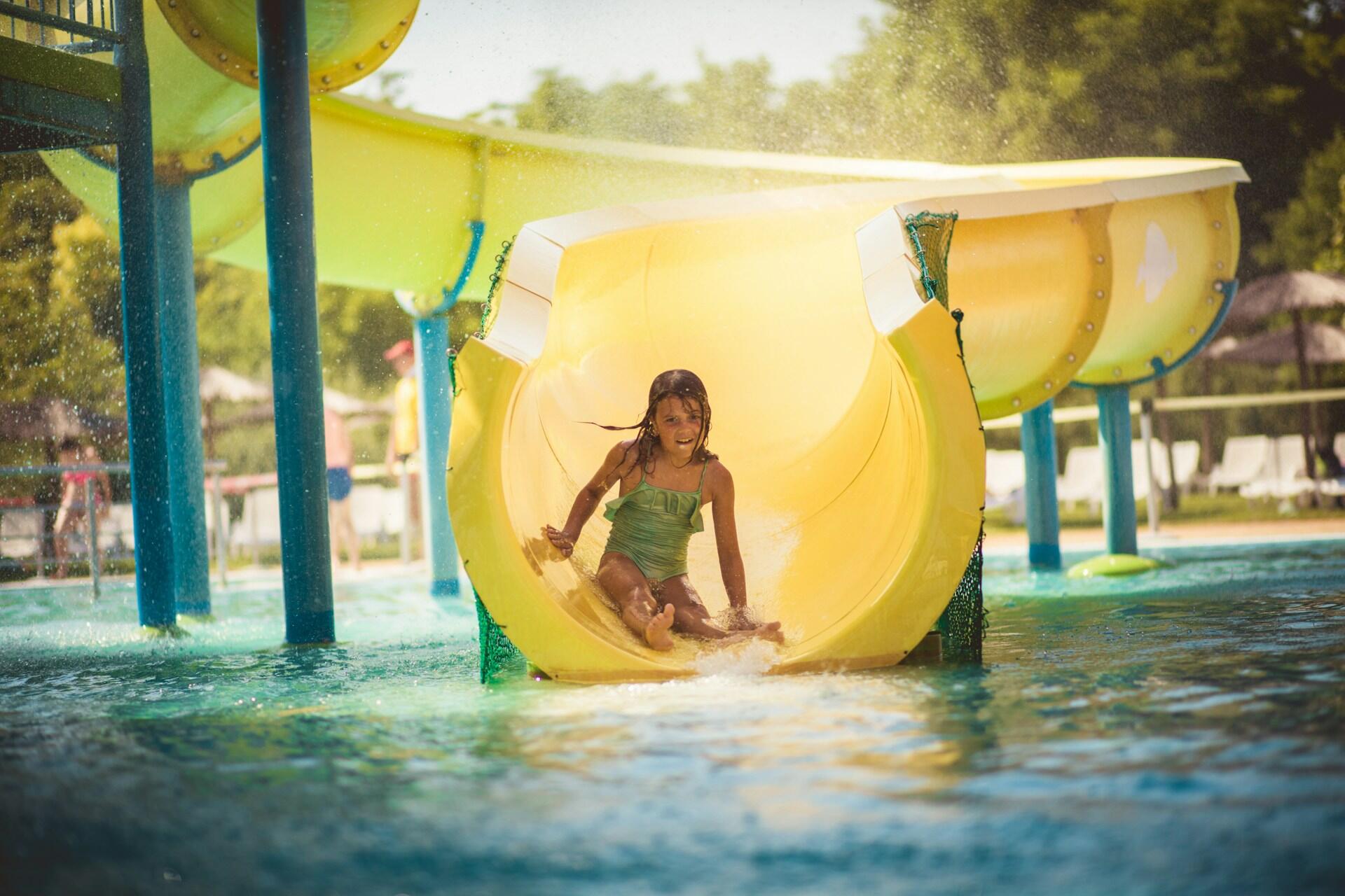 A child slides down a yellow pool slide on a sunny day.
