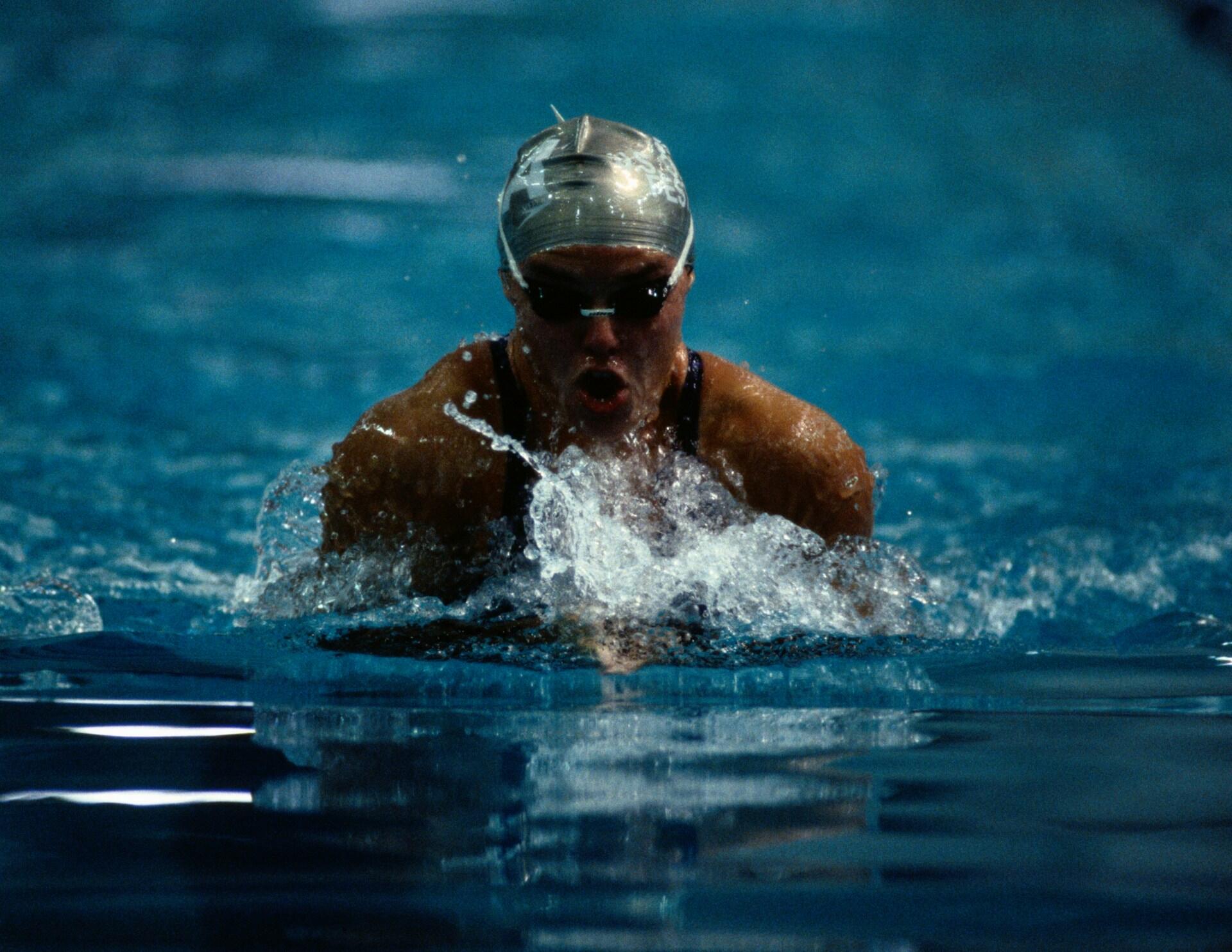 A person wearinng a swim cap and goggles swims in a pool.