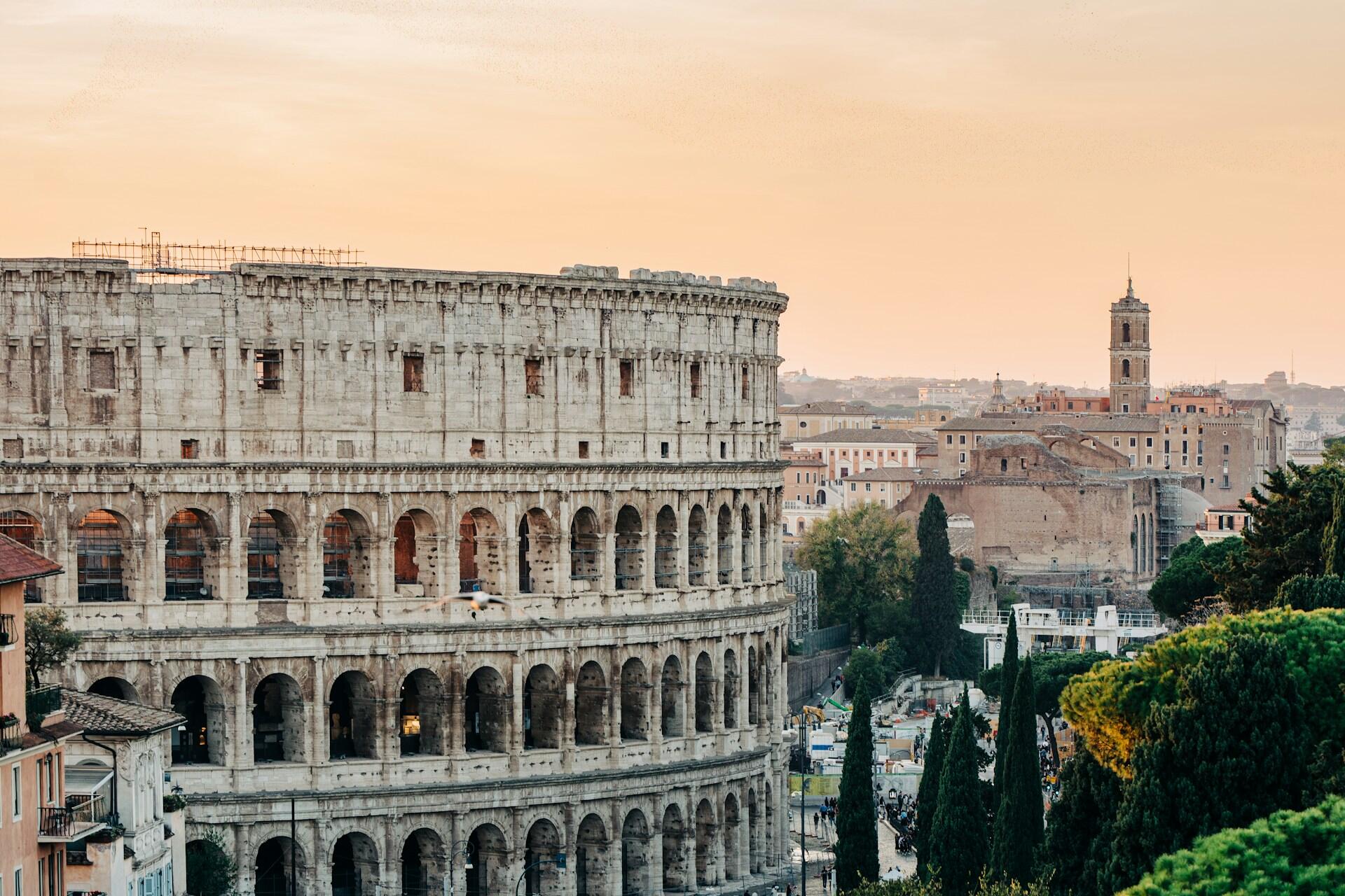 A view of the Colosseum in Rome with surrounding ancient architecture at dusk.