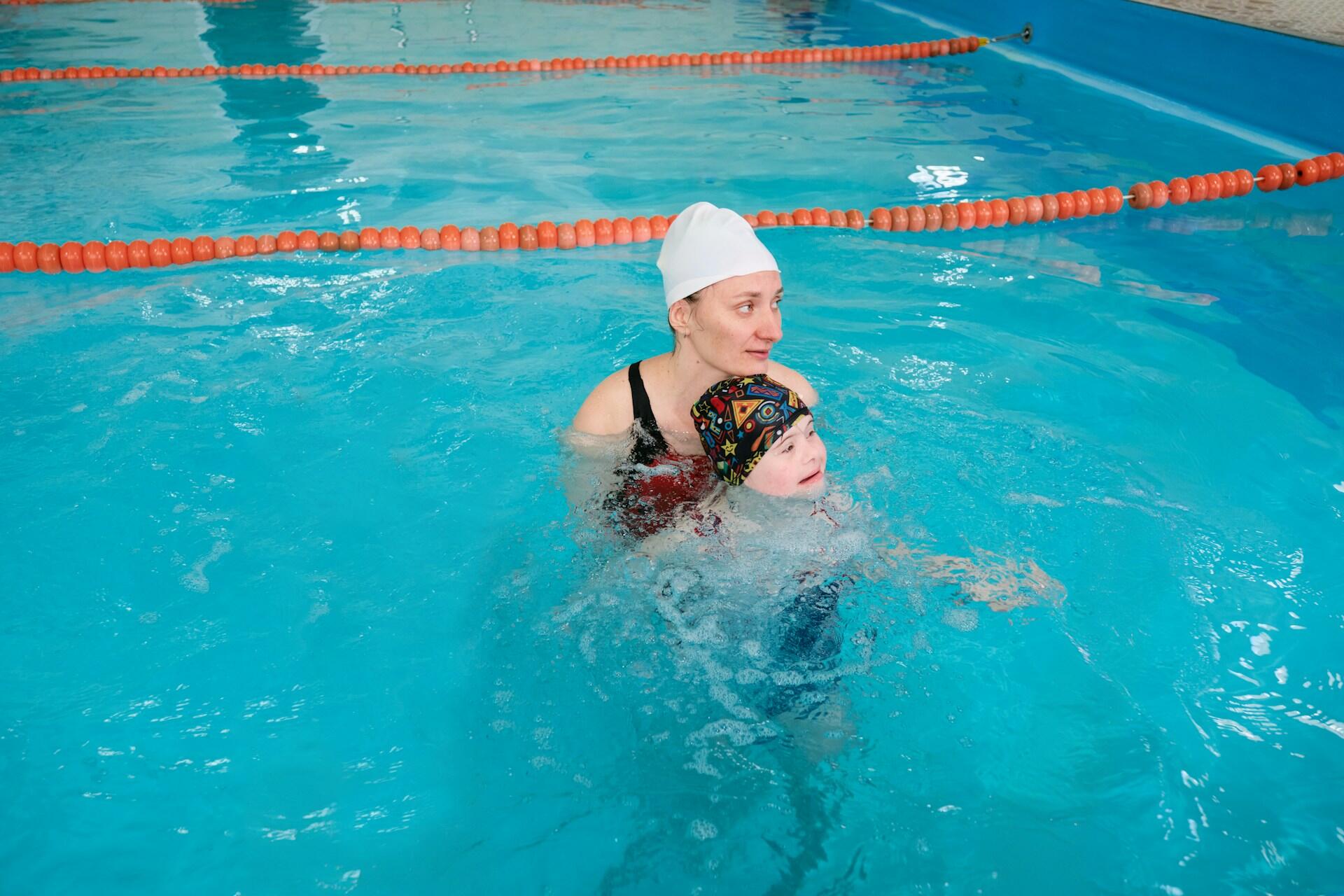 A person wearing a white bathing cap supports a child in a pool.