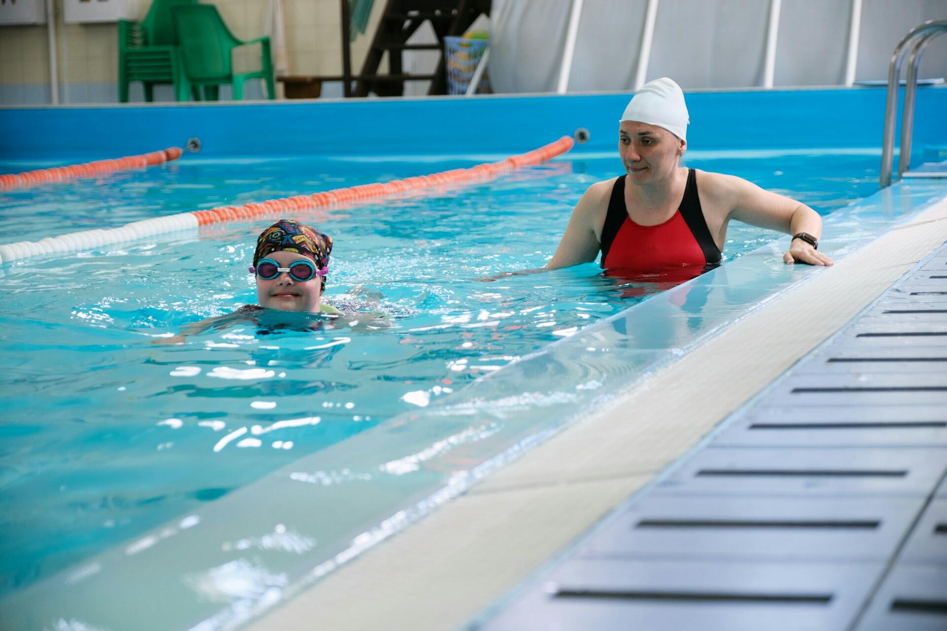 A woman in a pool overseeing a child swimming.