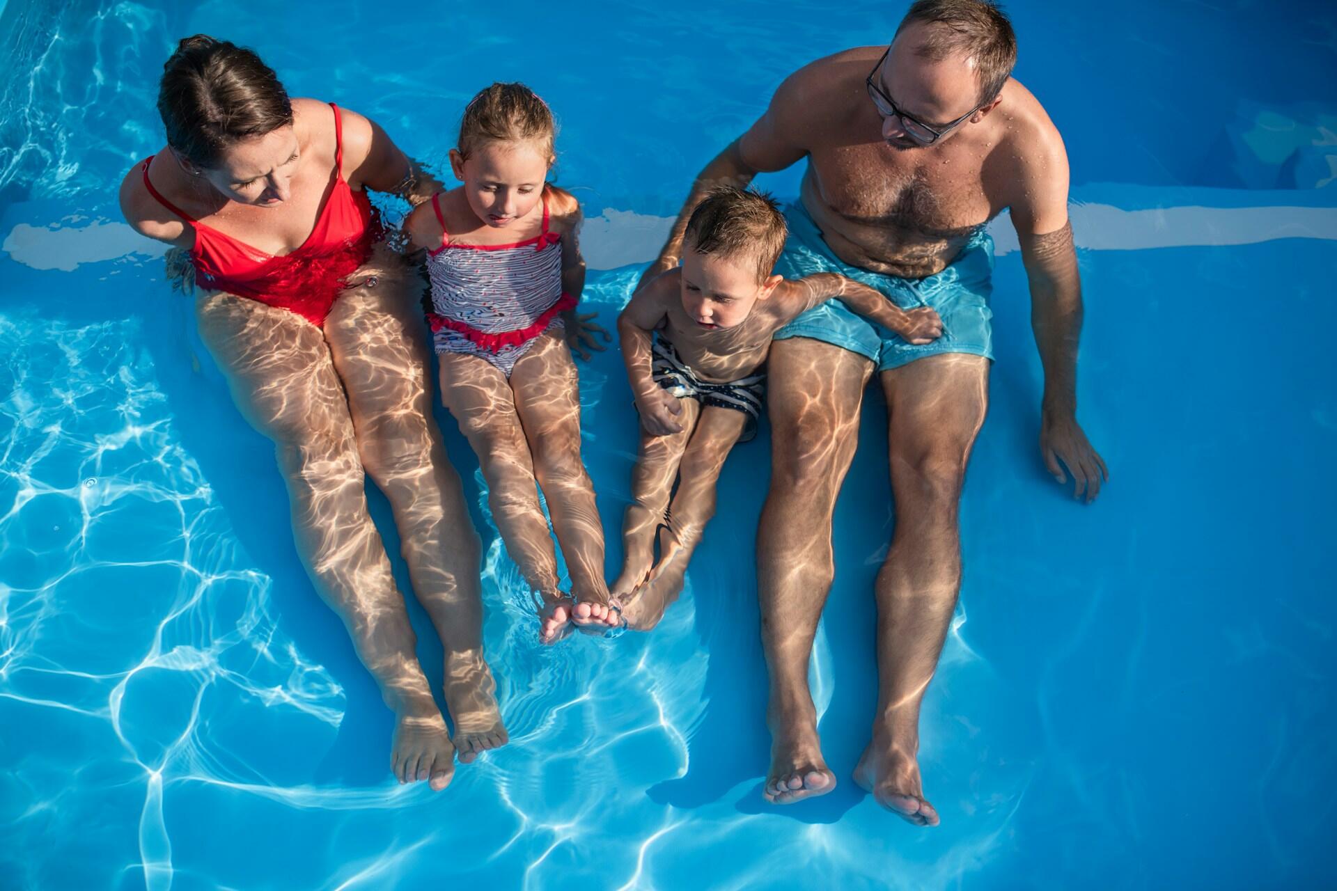 Two adults and two children sit in a pool.