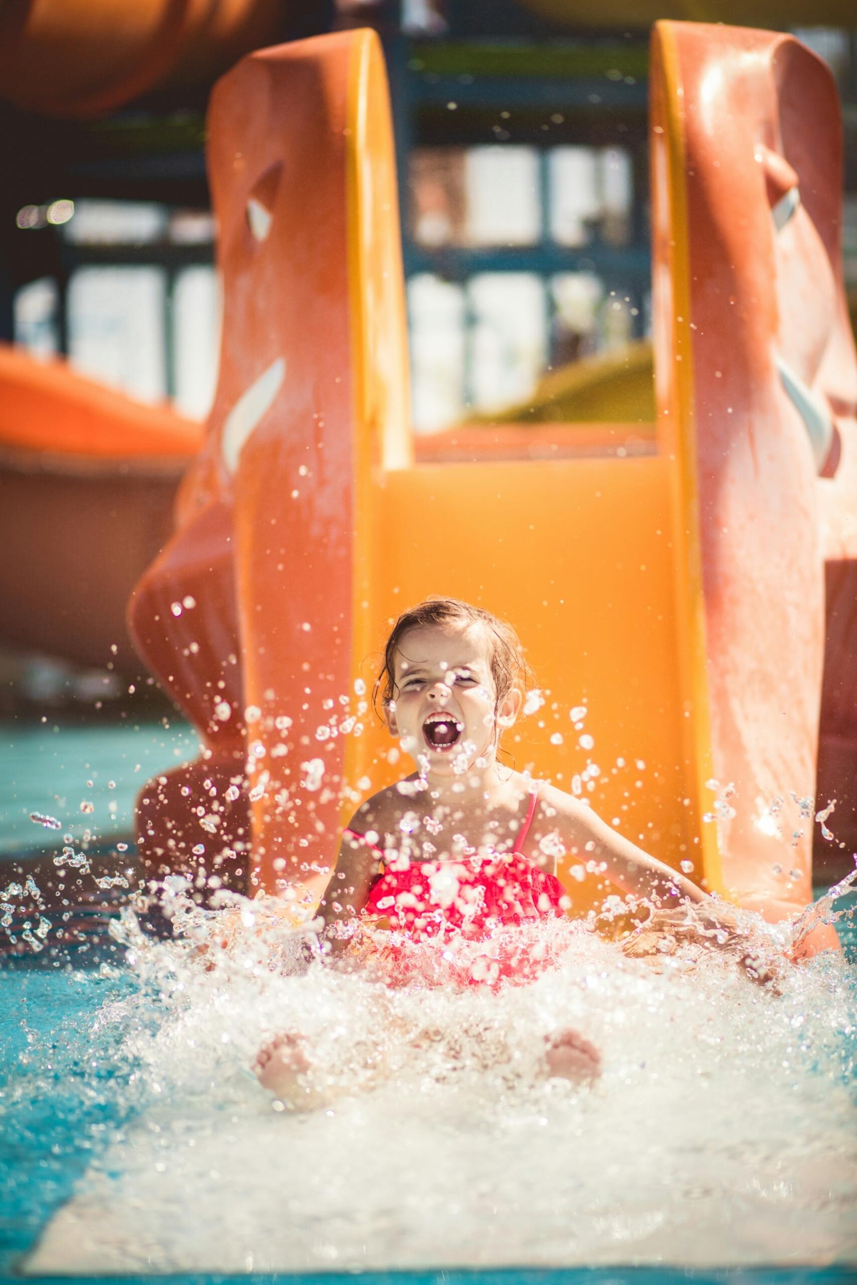 A child slides down an orange water slide on a sunny day.